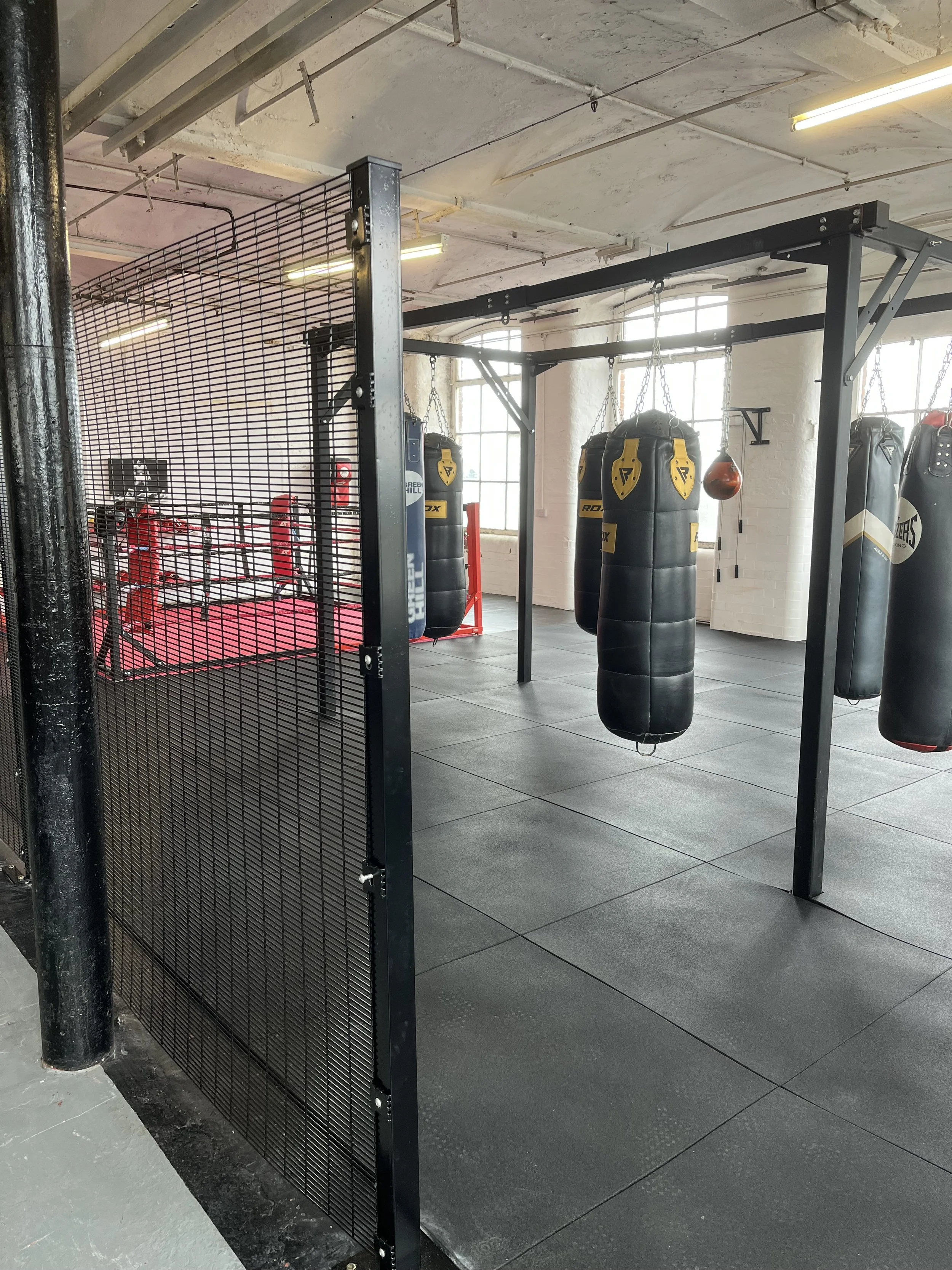 Boxing gym with punching bags, boxing ring, and gym flooring.