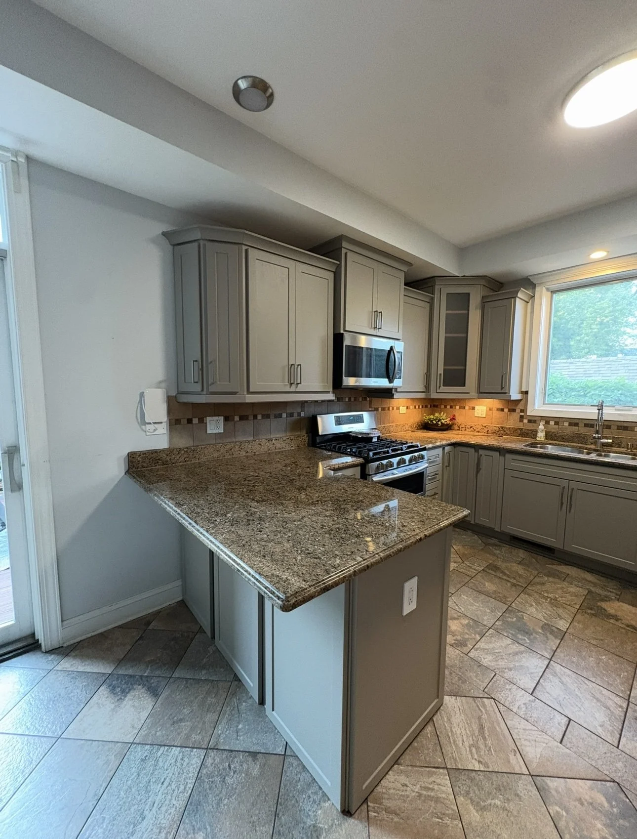 Kitchen with beige cabinets, granite countertops, stainless steel appliances, a window overlooking greenery, and tiled floors.