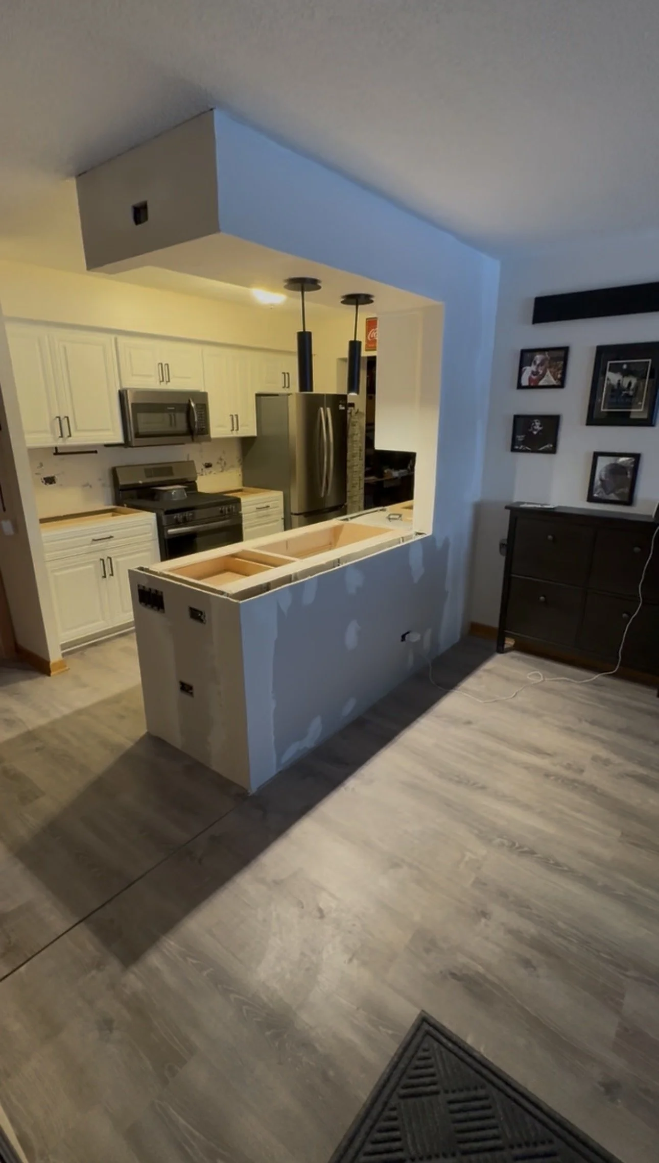 Kitchen with white cabinets, stainless steel appliances, and a partially built counter with drywall and electrical outlets, viewed from the living room with hardwood flooring.