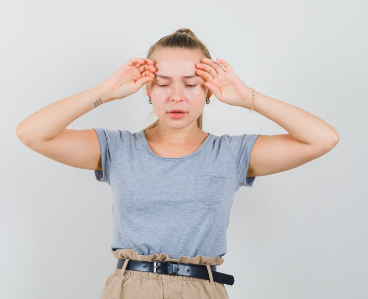 Young woman with blonde hair in a ponytail holding her head with both hands and a worried expression.