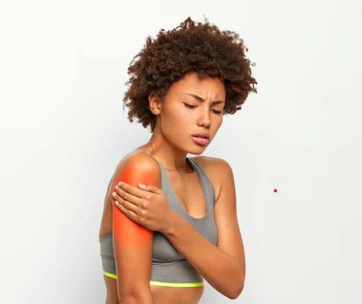 Young woman with curly hair experiencing shoulder pain, touching her right shoulder with a concerned expression.