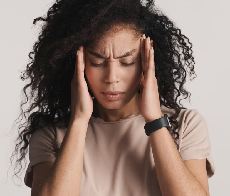 Young man in a grey polo shirt and beige pants sitting on a bench with shadow cast on a beige wall.