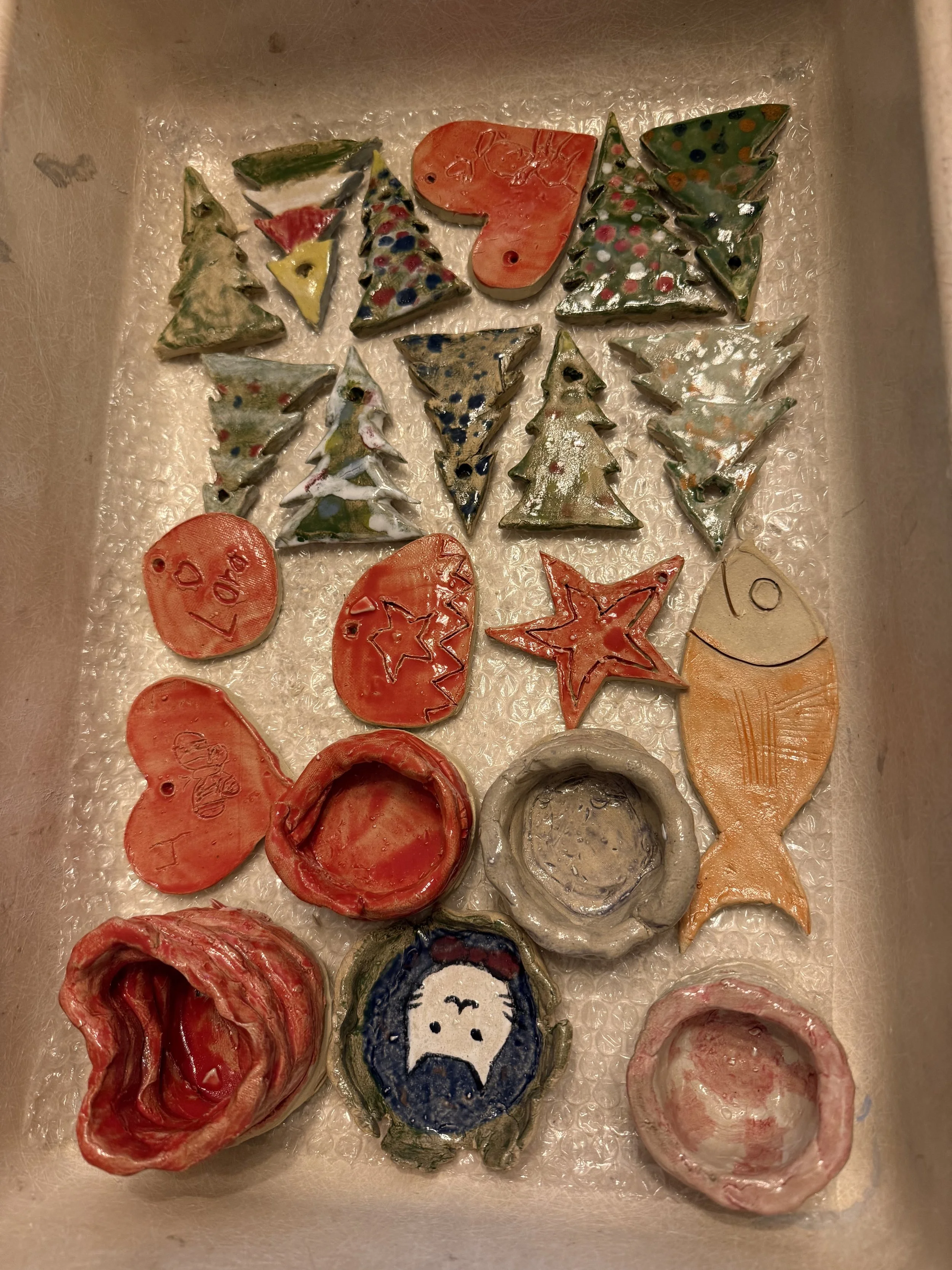 A tray with various painted and decorated seashells featuring Christmas-themed designs, such as trees, stars, hearts, and a snowman.