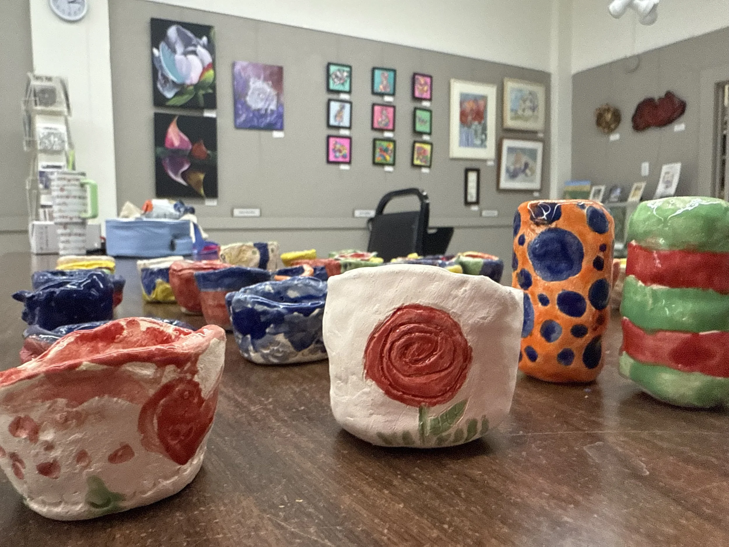 Colorful handmade paper mâché bowls with painted designs on a wooden table inside an art gallery or classroom.