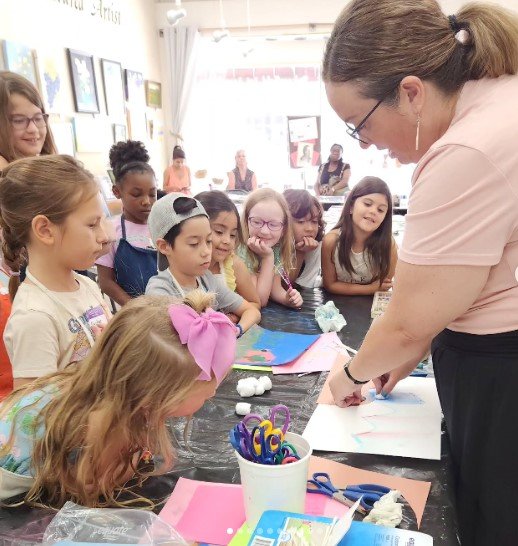 Teacher demonstrating craft activity to group of children in classroom.