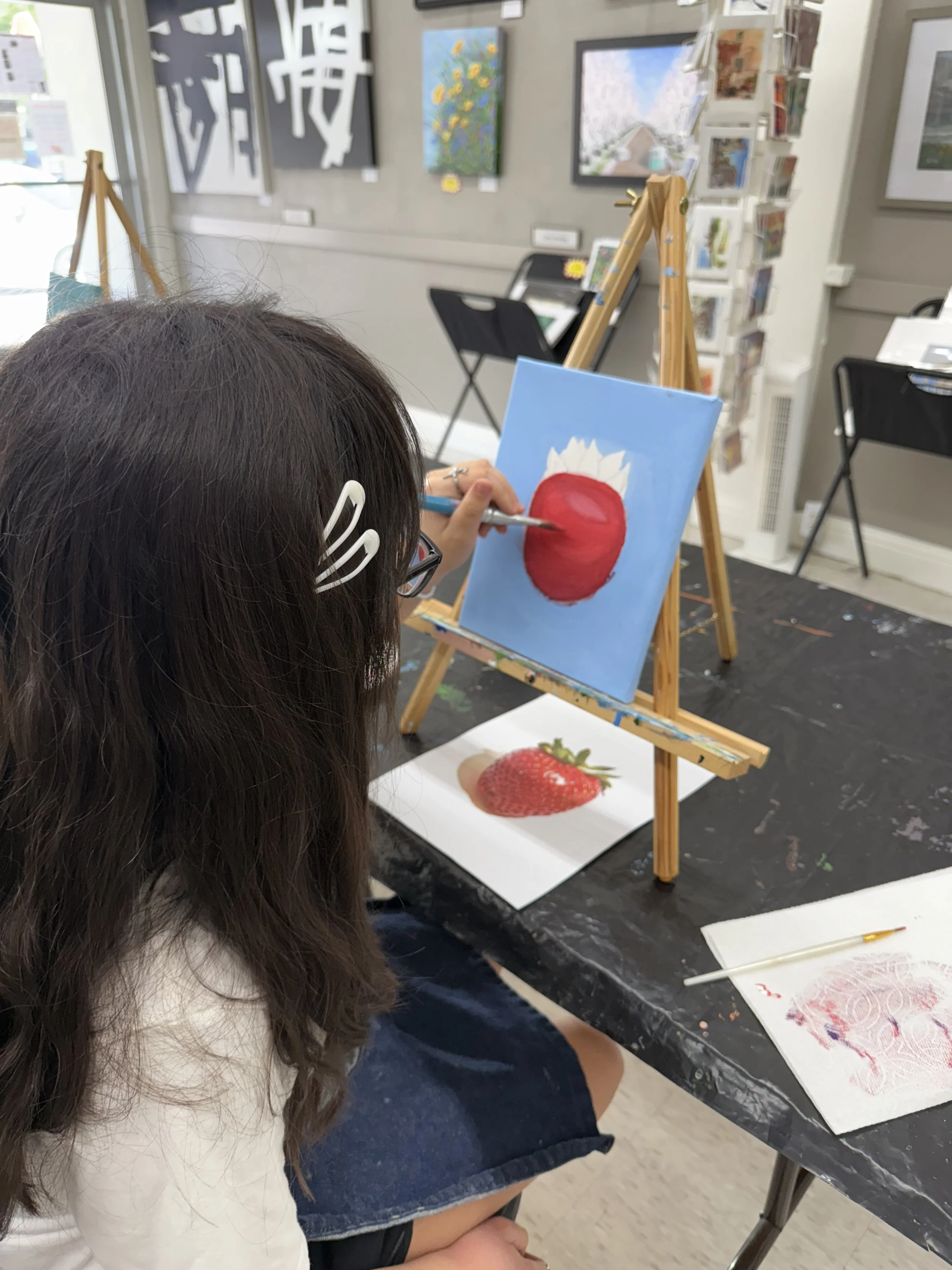 A woman painting a strawberry on a canvas in an art gallery.