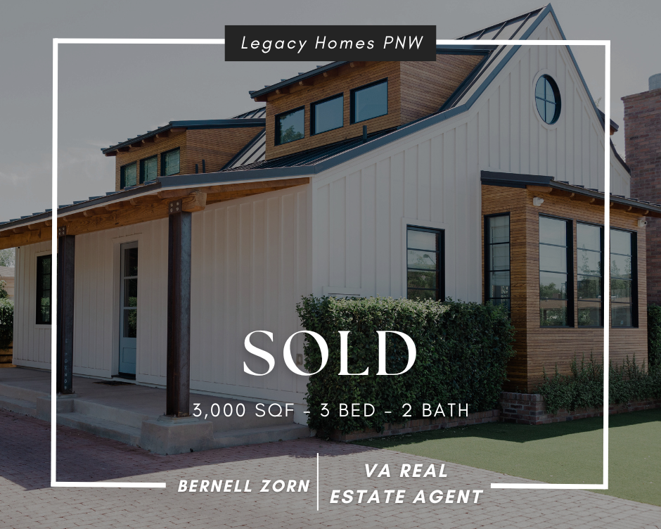 Modern house with white and wooden exterior, large windows, and a small front porch, with overcast sky.