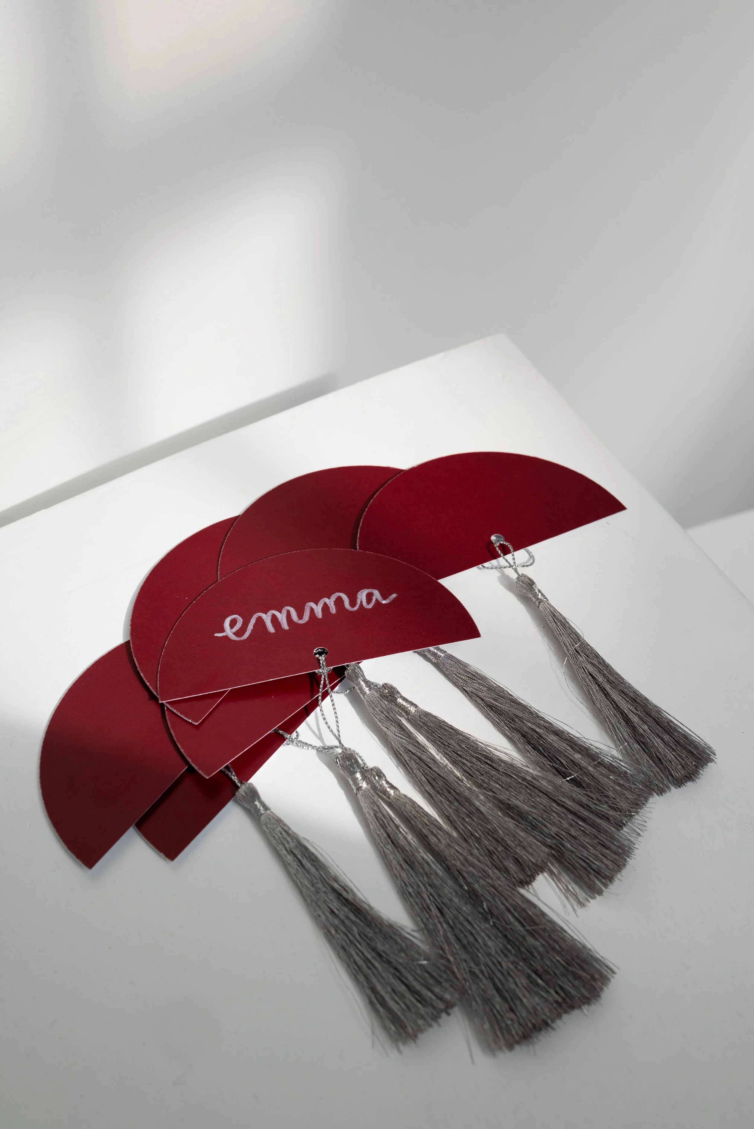 Set of red semi-circular cards with silver tassels and one card has the name "emma" written on it.