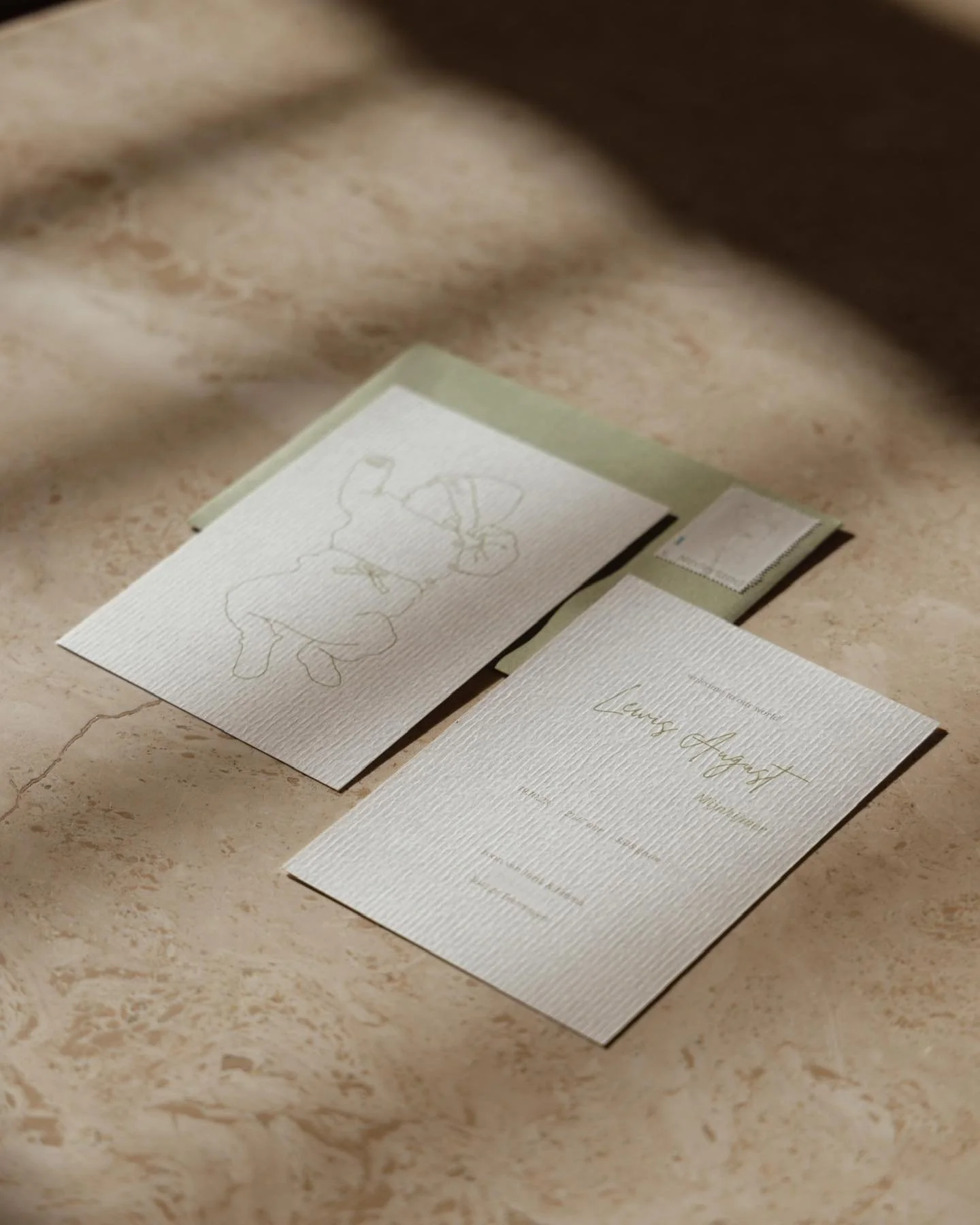 Een trouwuitnodiging en een bijpassende RSVP‑kaart met elegante gouden lettering op structuurpapier, geplaatst op beige marmer.