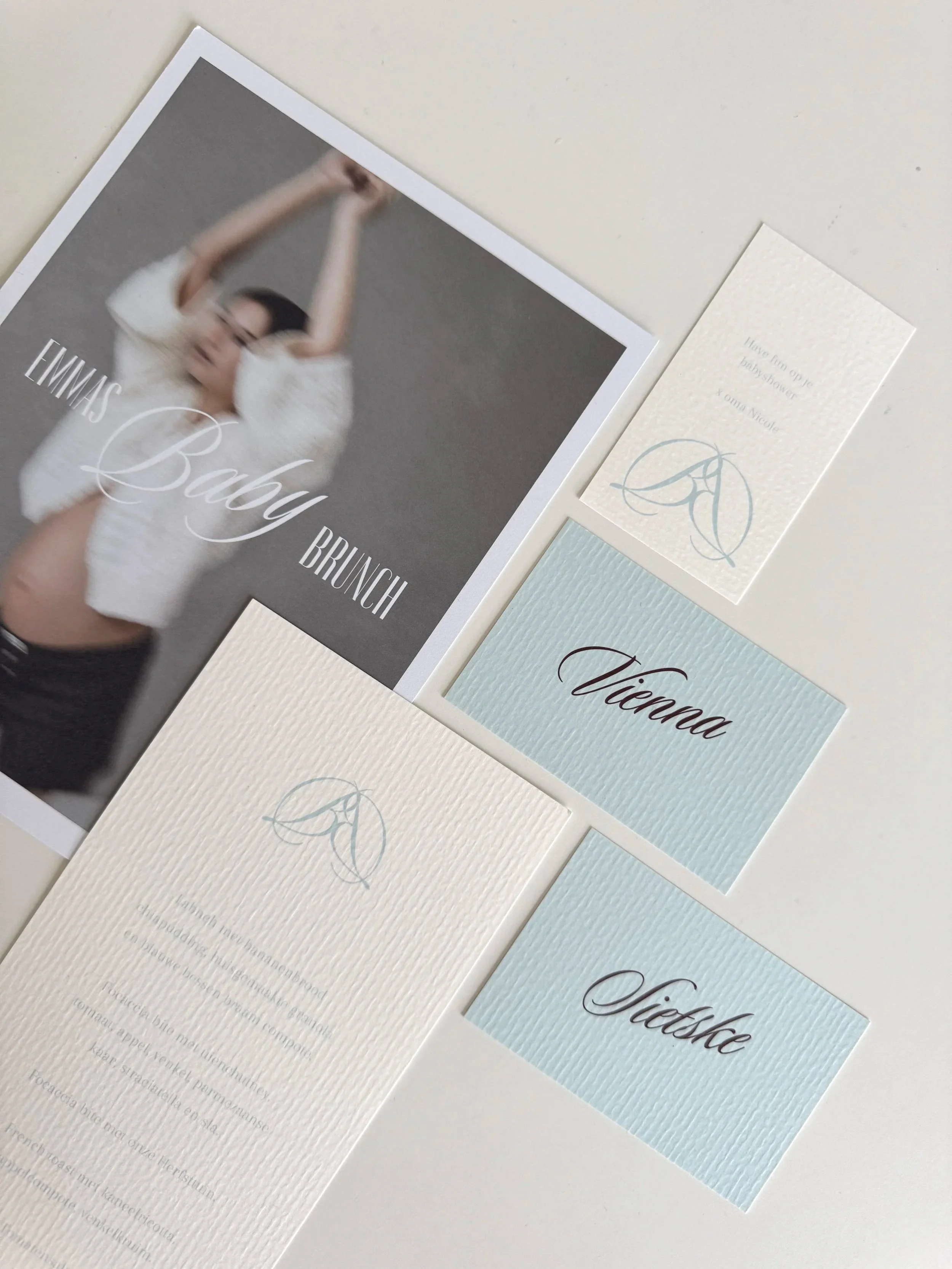 Uitnodiging voor Emma’s Baby Shower brunch met een vervaagde foto van een vrouw, naast kleine kaartjes met de namen Victoria en Lisette, op een witte achtergrond.