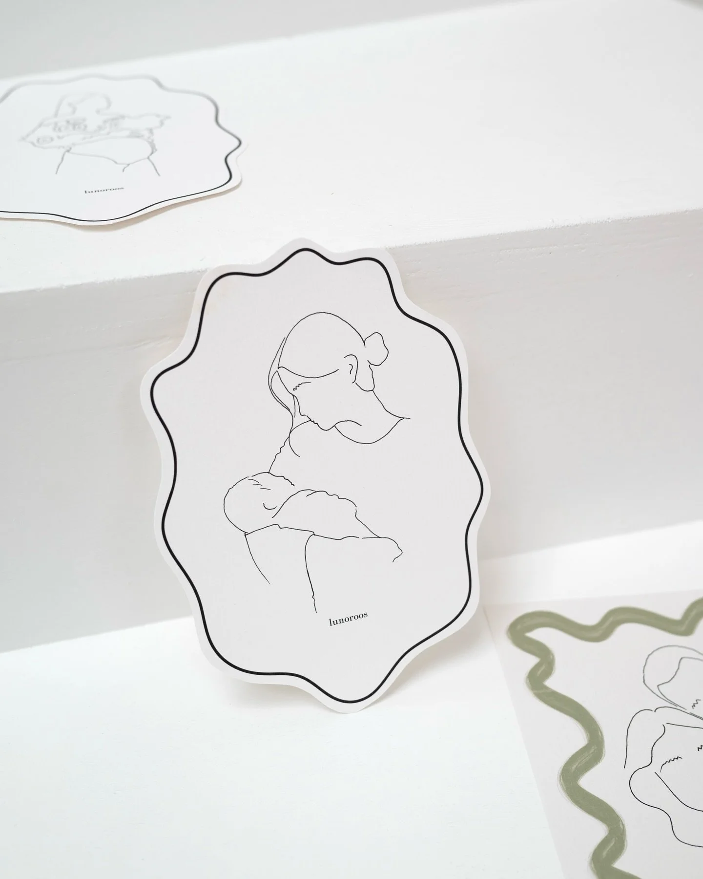 Lijntekening van een vrouw die een baby vasthoudt, met het woord ‘lunoroos’ onderaan.