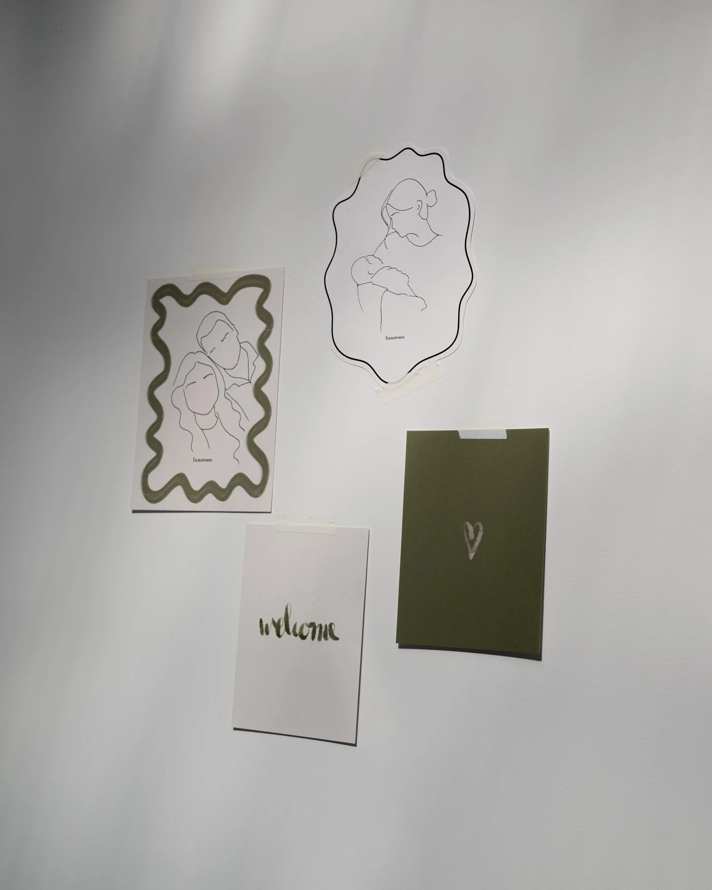 Decoratieve wand met minimalistische lijntekeningen van twee personen, een fotolijst en twee kaartjes met de woorden ‘welcome’ en een hartje.