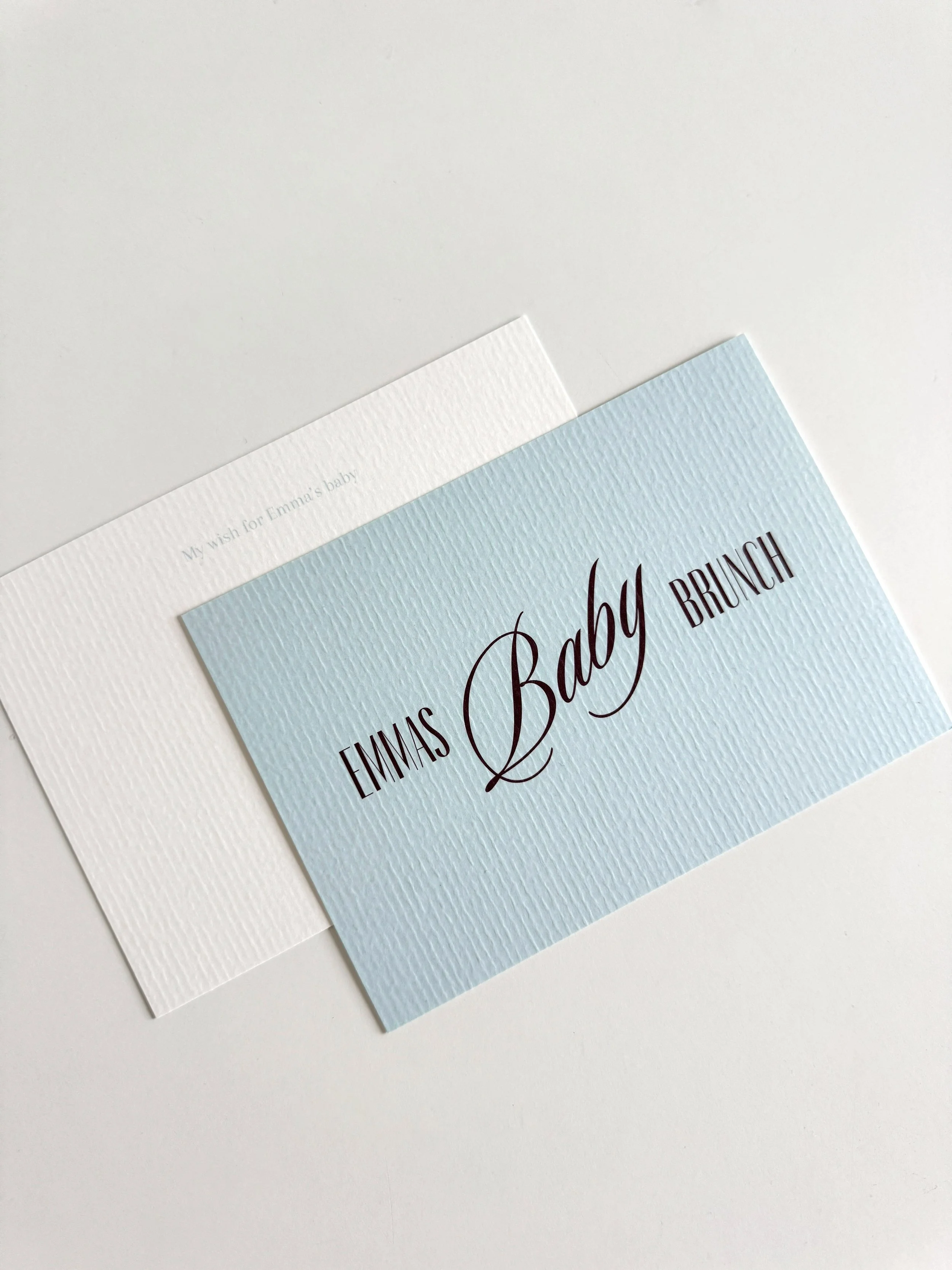 Een blauwe en witte kaart met textuur en elegante tekst ‘Emma’s Baby Brunch’ en daaronder ‘My wish for Emma’s baby’.