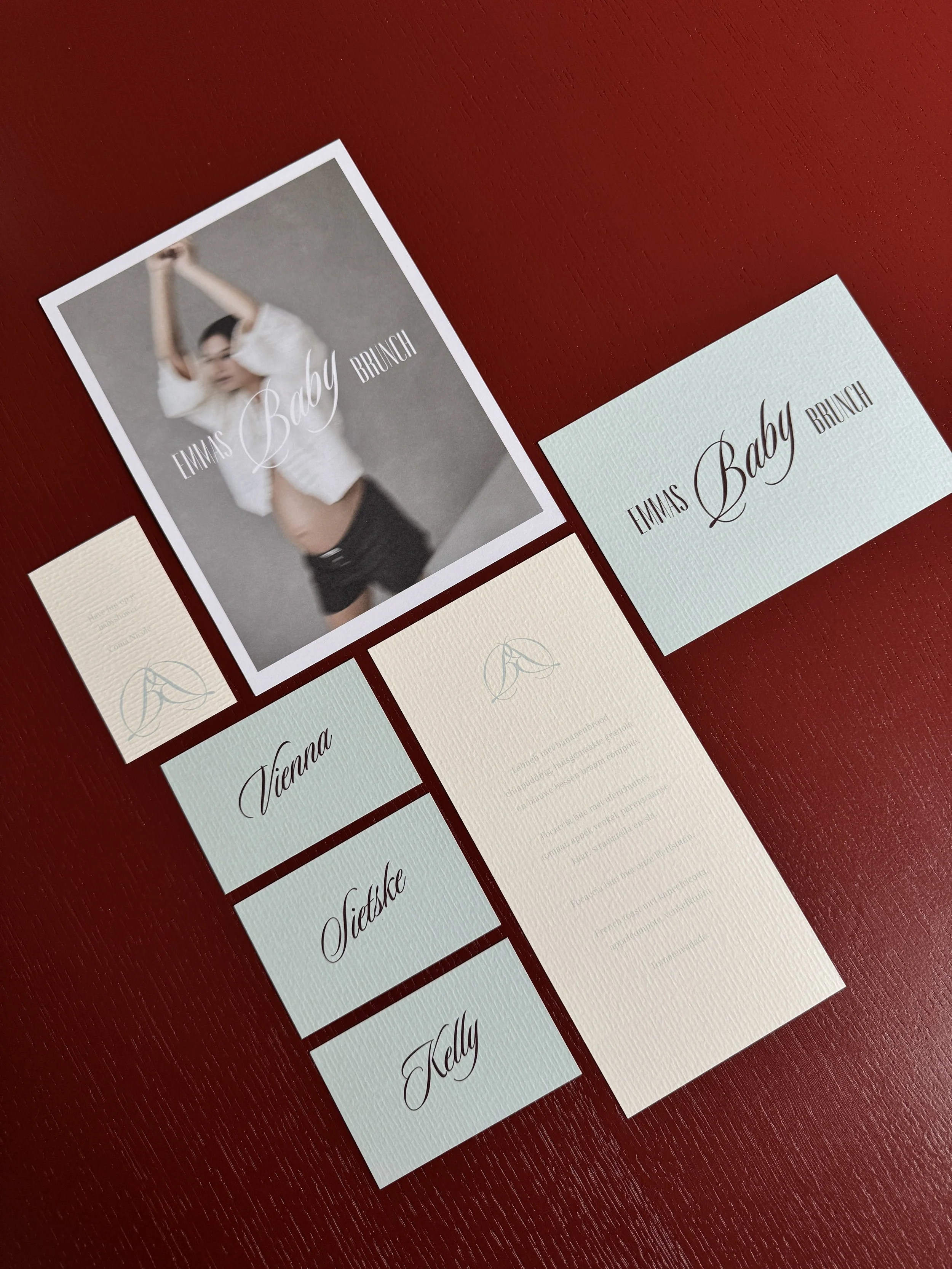 Uitnodiging en naamkaartjes voor Emma’s Baby Brunch, met een foto van een vrouw die zich uitstrekt en haar armen omhoog doet, geplaatst op een donkerrode ondergrond.