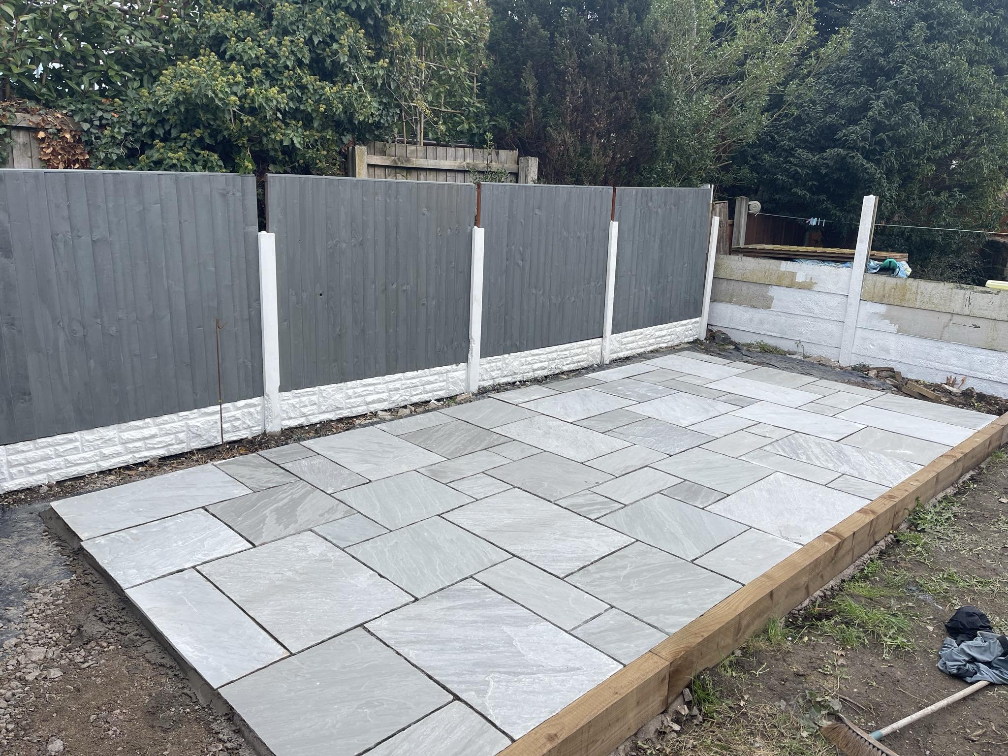 Slate tiles being installed on a wooden frame in a backyard, with a grey fence and trees in the background.
