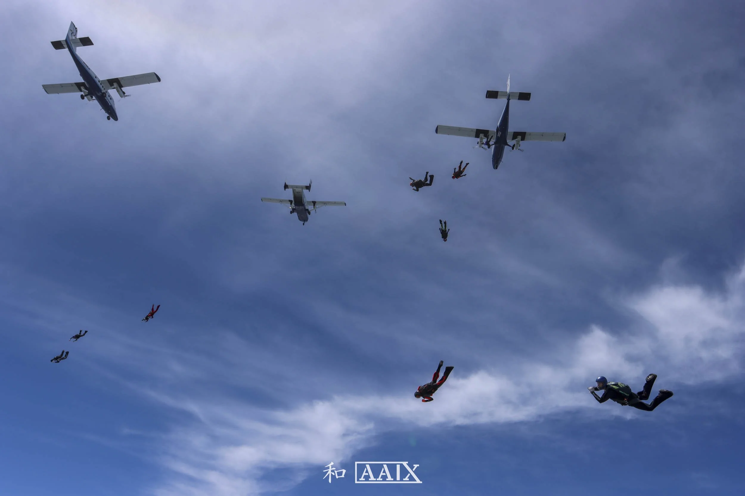 Skydivers falling from aircrafts in the sky with clouds in the background.