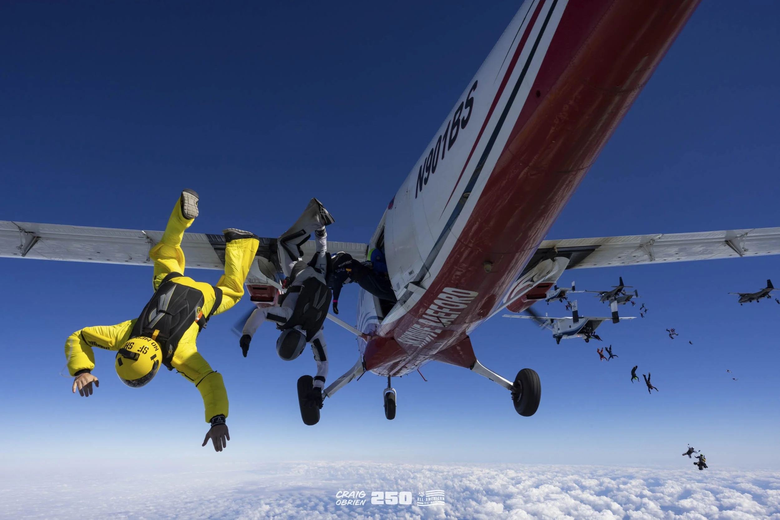 Skydivers exiting an aircraft over the clouds during a jump in clear weather.