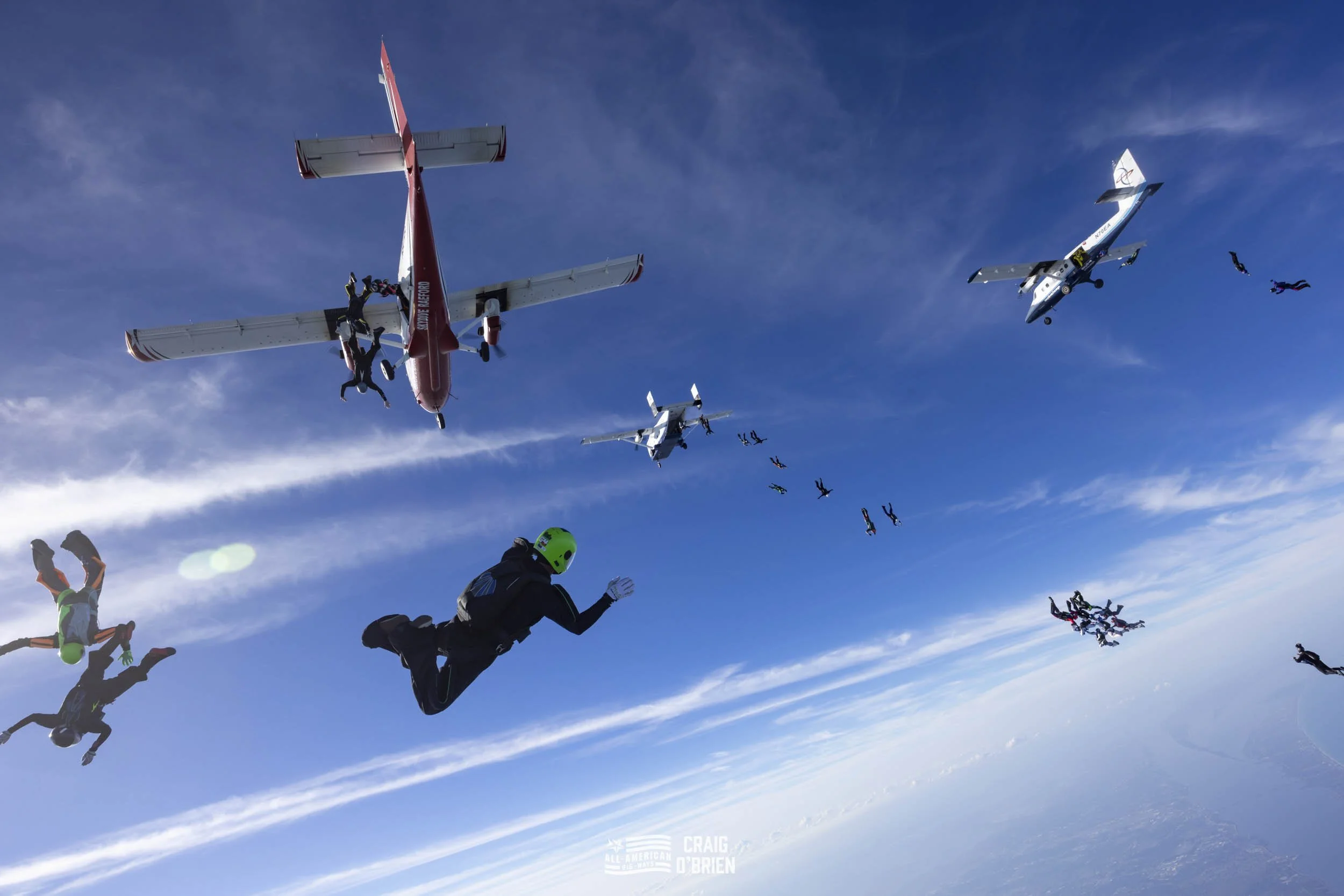 People skydiving from airplanes high above the earth with a blue sky and clouds in the background.