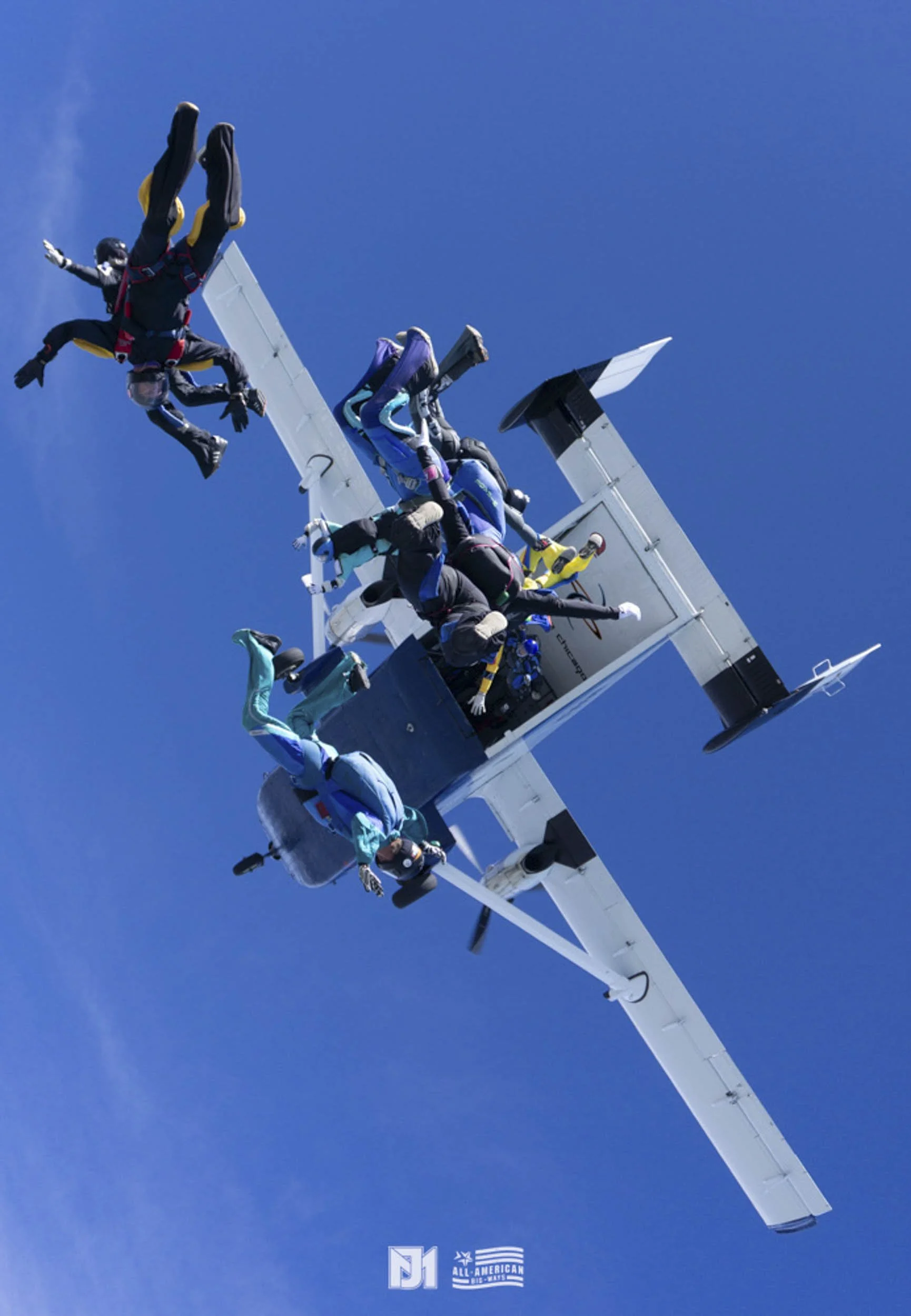 Group of skydivers jumping out of an airplane against a clear blue sky.