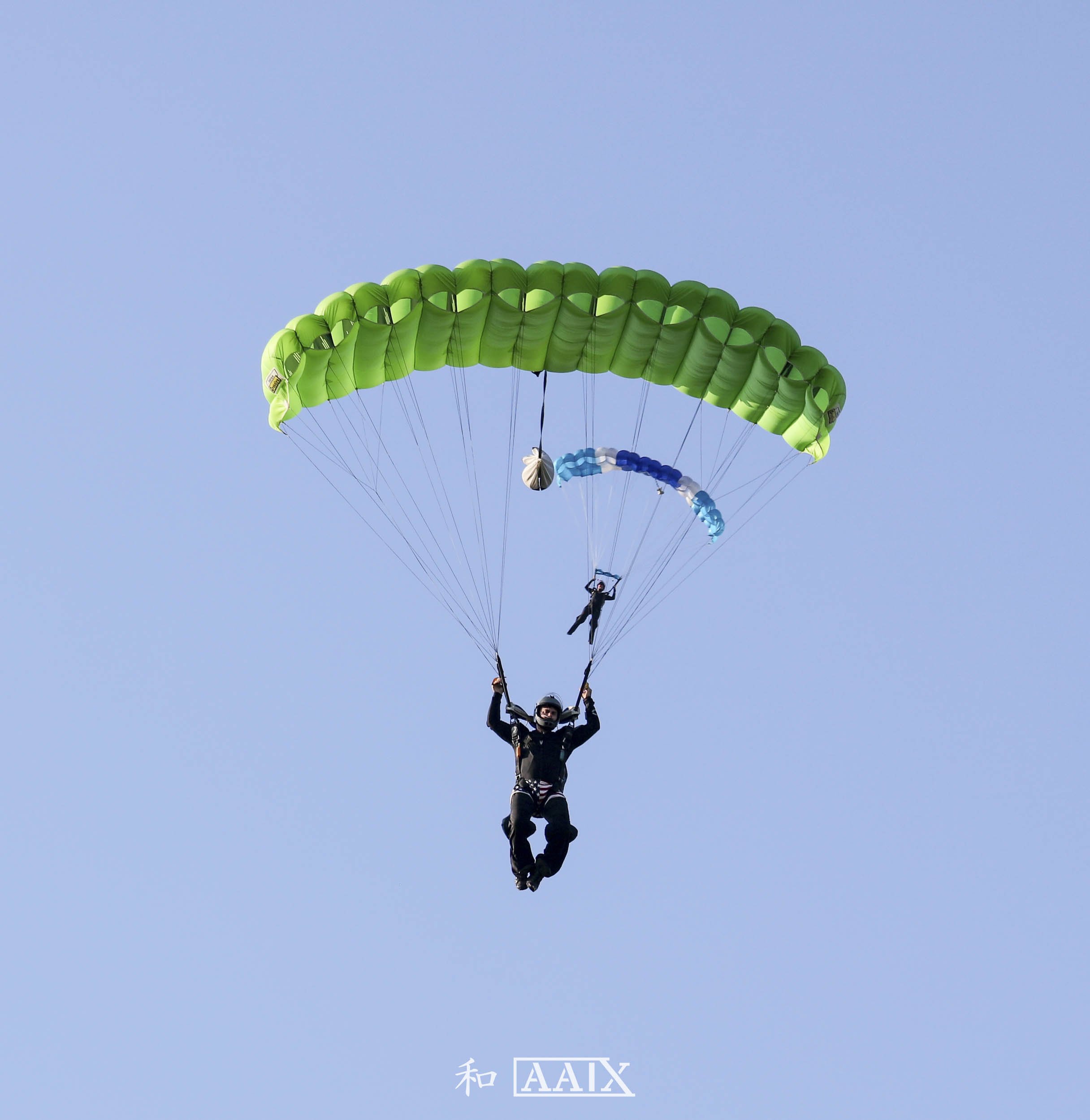 Person skydiving with a green parachute in clear blue sky.