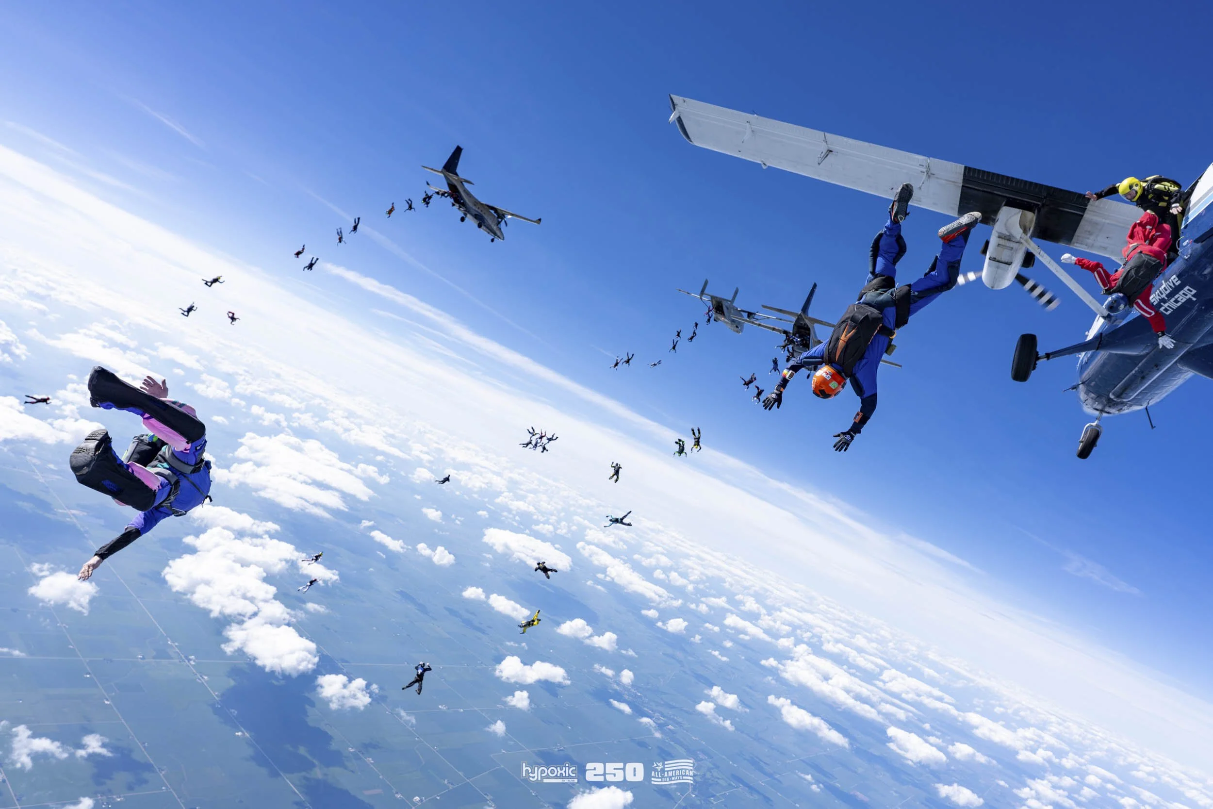 Skydivers jumping from airplanes in mid-air over a cloudy sky.
