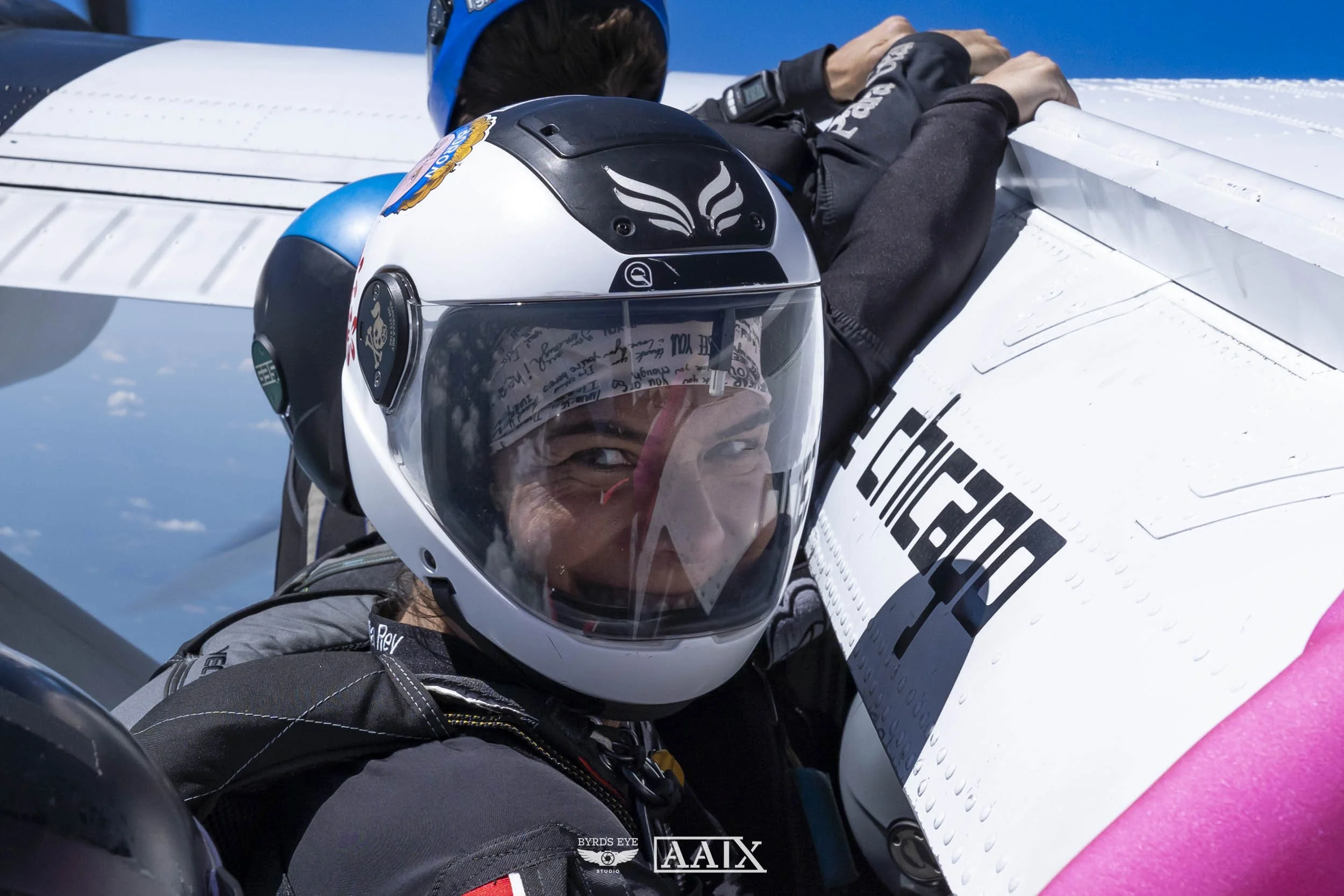 A smiling female astronaut in a space helmet sitting in a spacecraft, with Earth visible in the background.