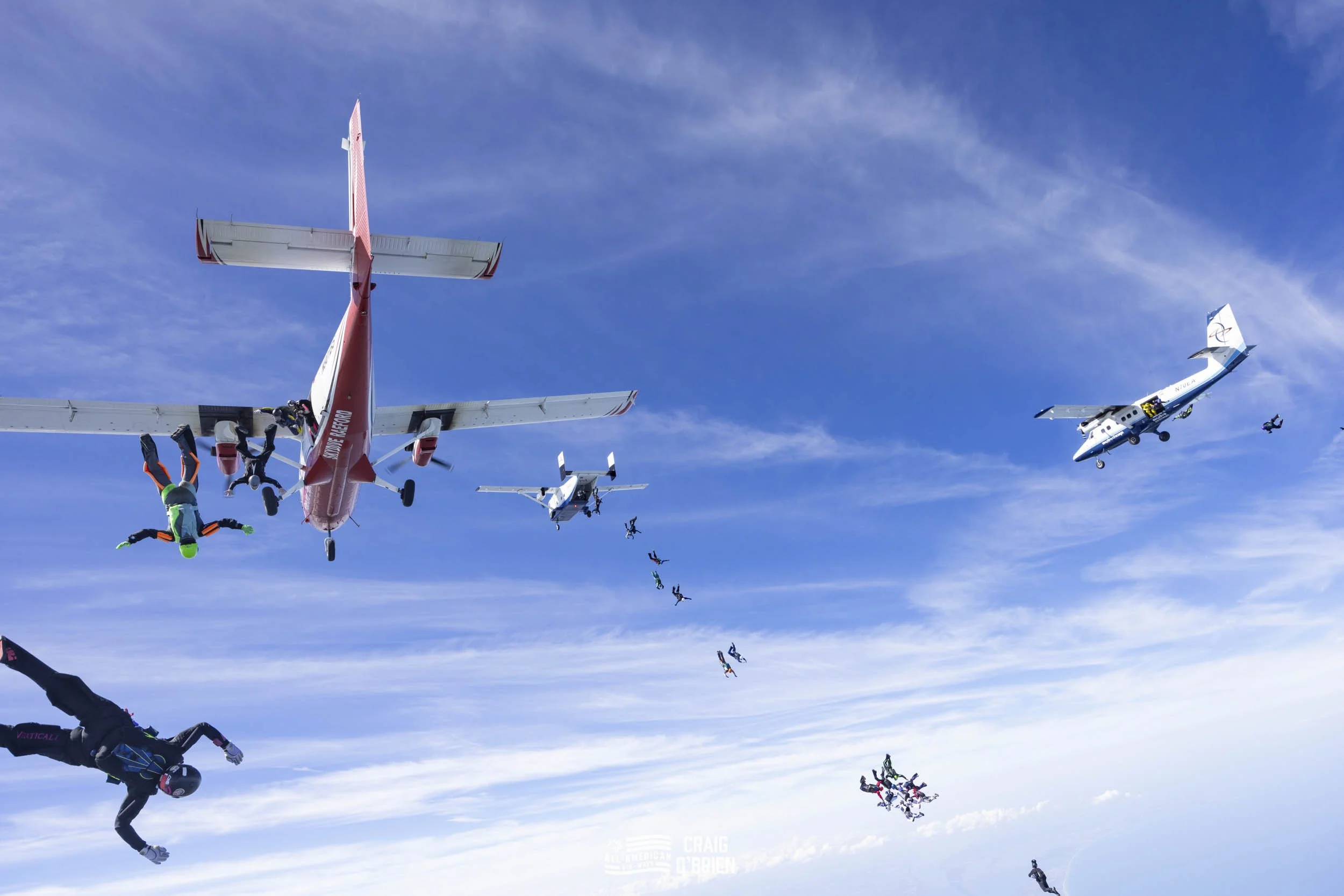 Skydivers free-falling from a plane in the sky with blue and white clouds.