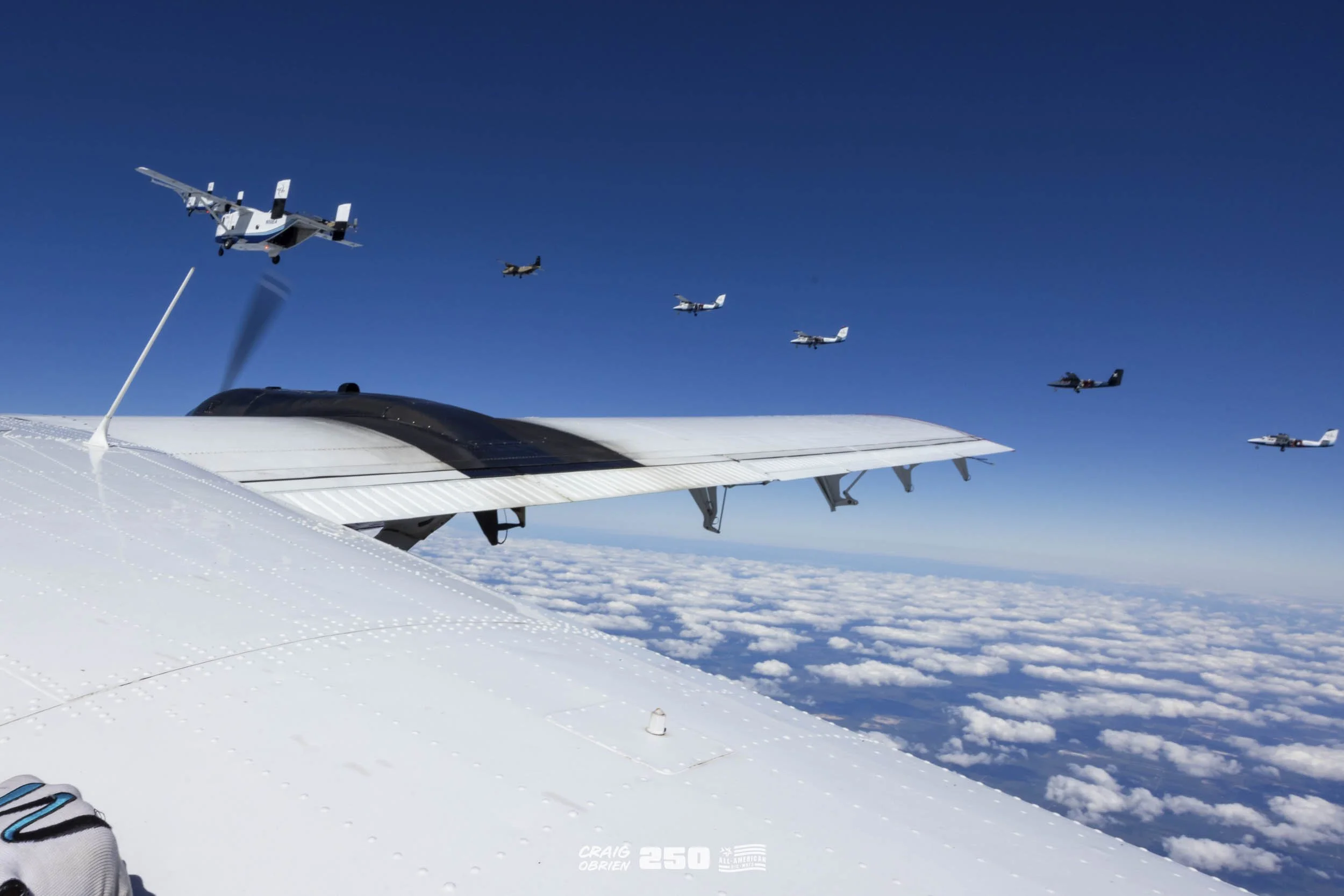Aerial view from an airplane showing several oth...s in formation above the clouds in a clear blue sky.