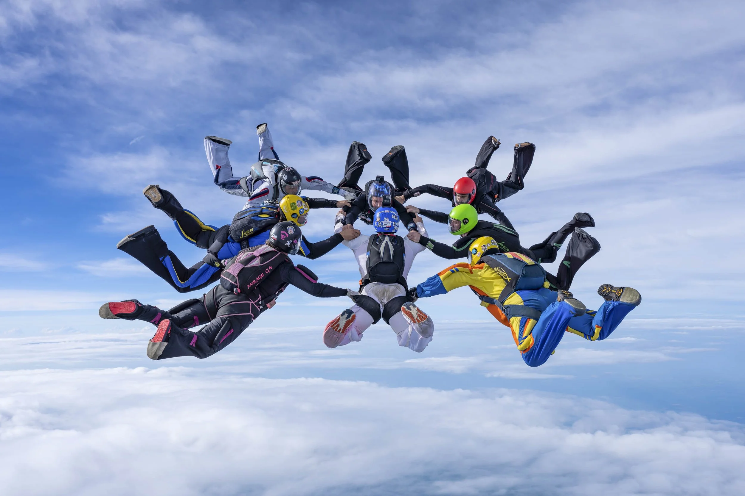 Multiple skydivers in freefall formation against a blue sky with clouds.