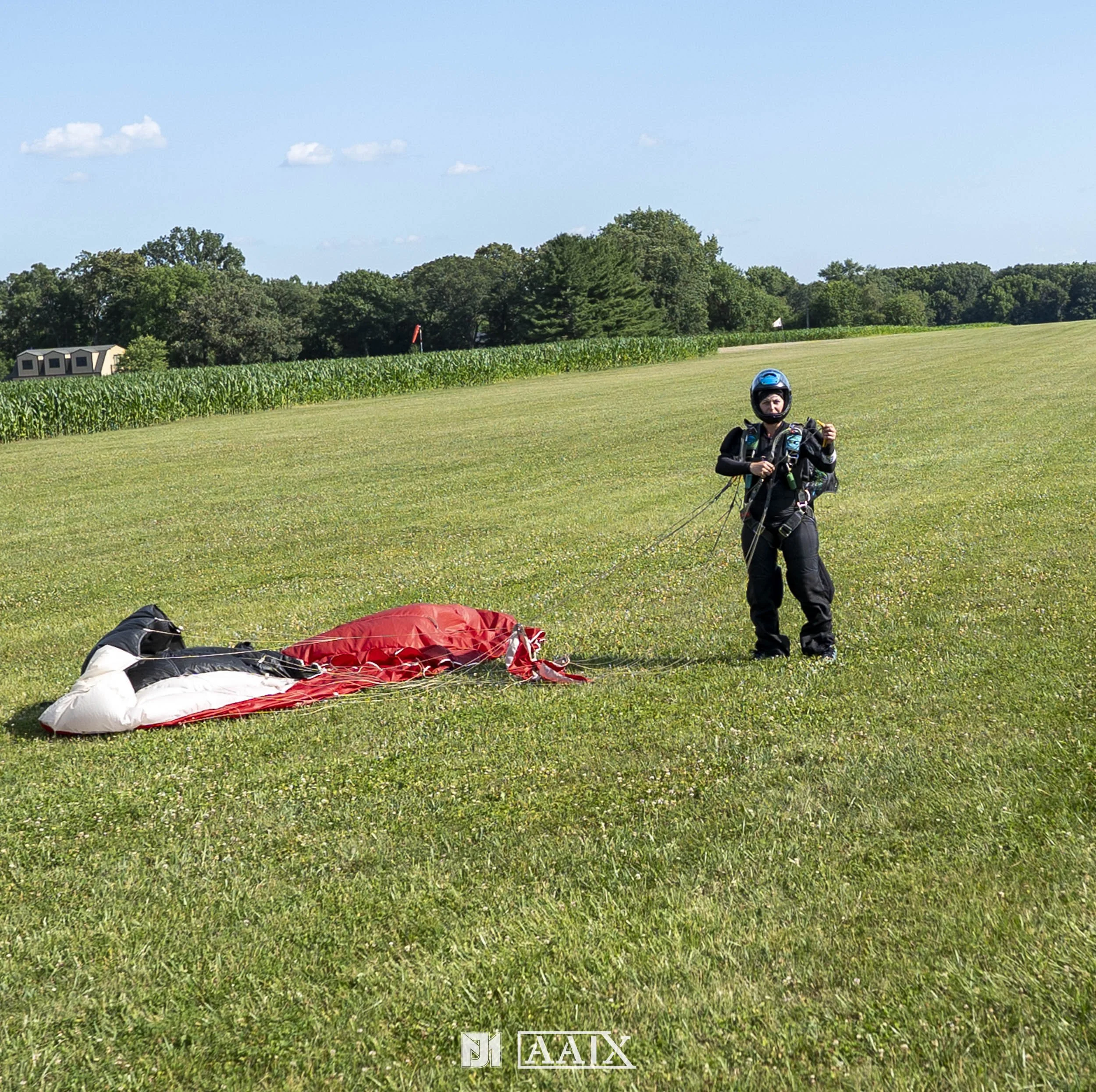 Person in skydiving gear standing on grassy field with parachute laid out on the ground.