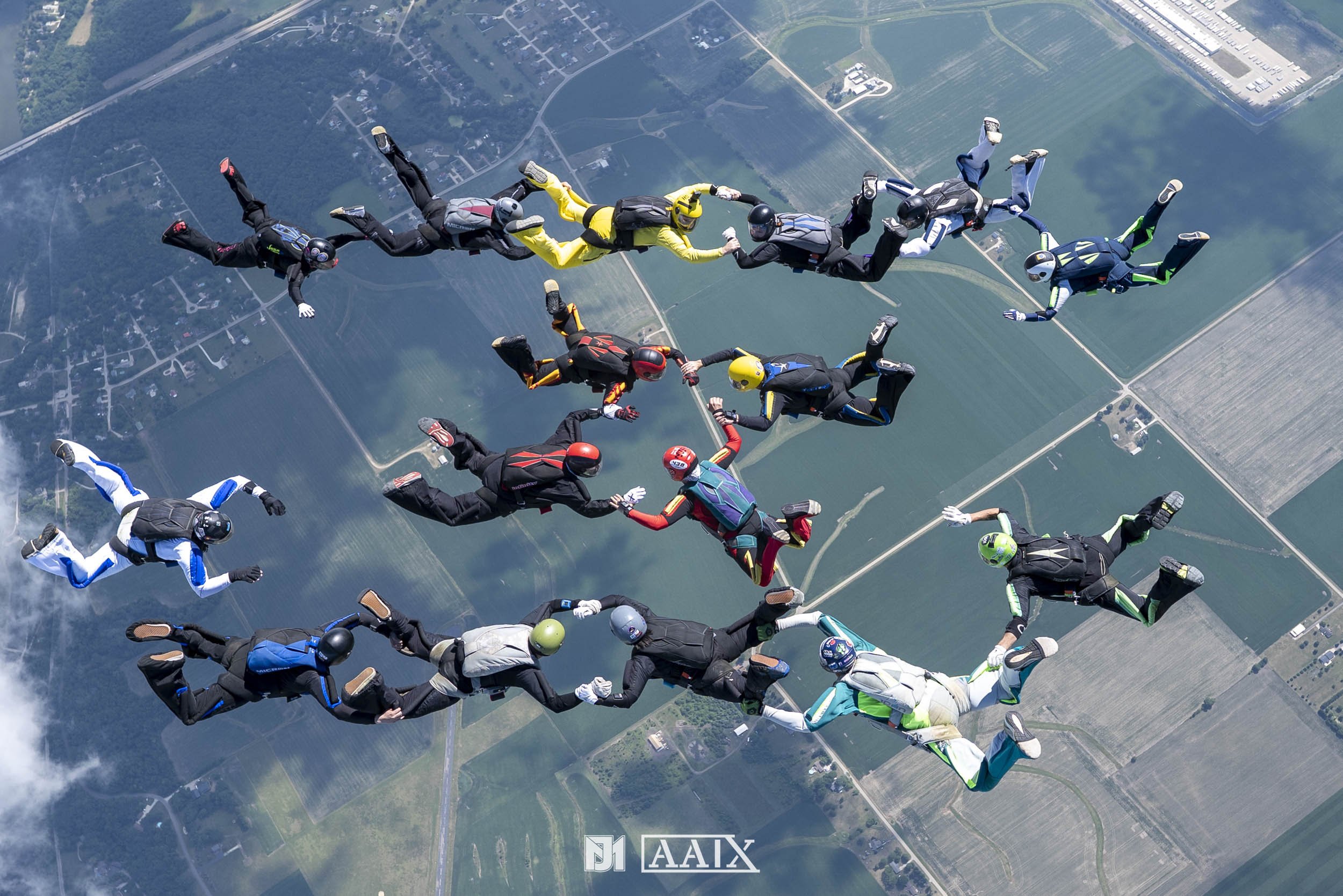 Group of skydivers holding hands while free-falling above farmland and fields.