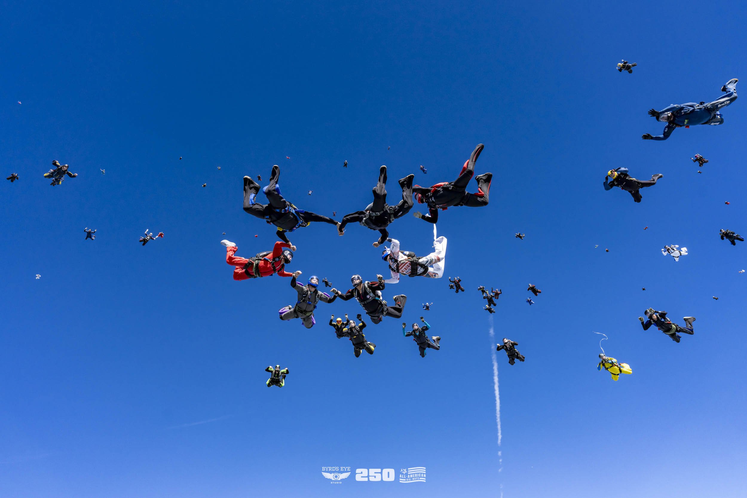 Multiple skydivers in free fall holding hands against a clear blue sky during a coordinated jump.