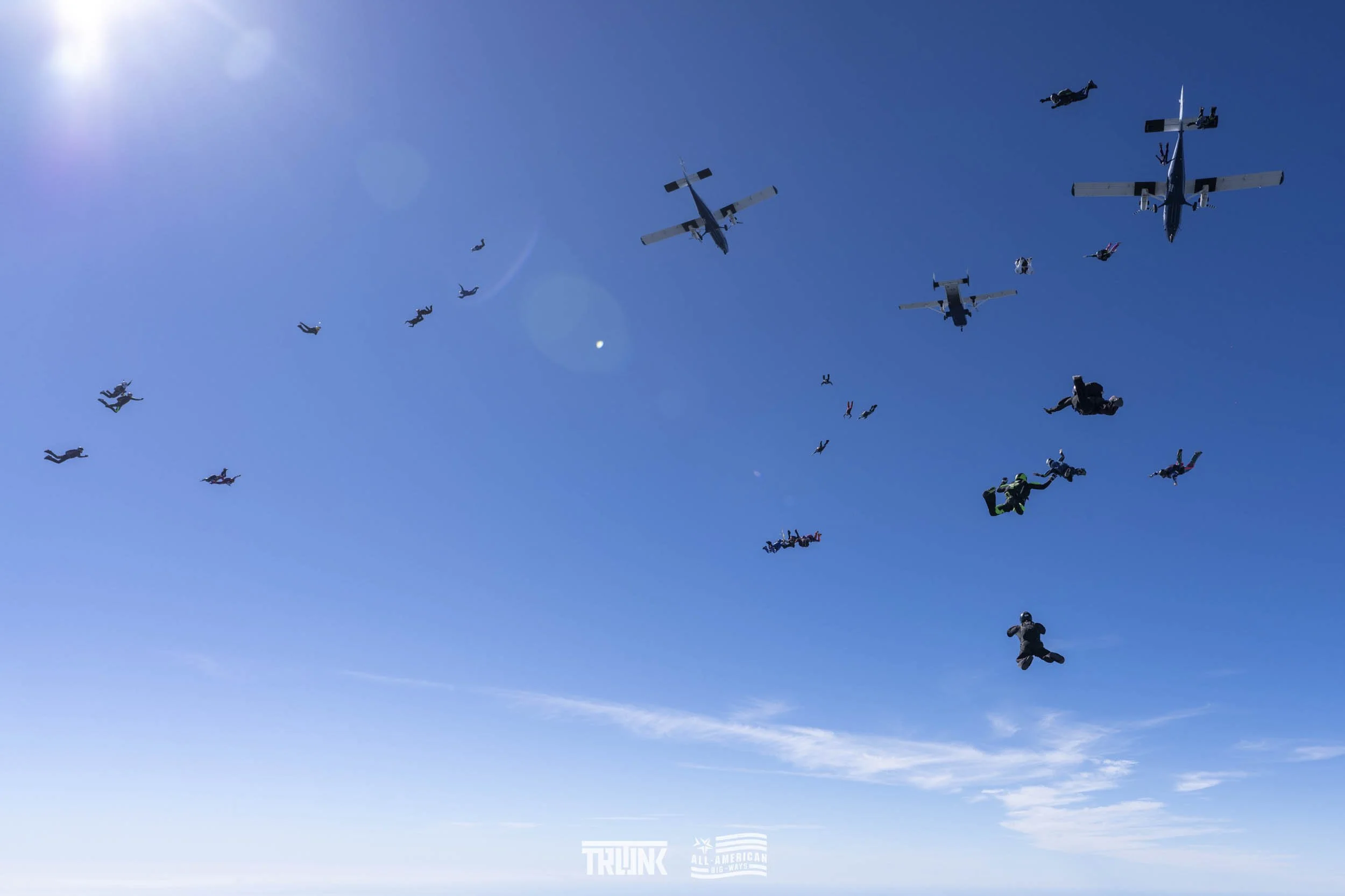 Skydivers in free fall formation with some aircraft flying in the clear blue sky.