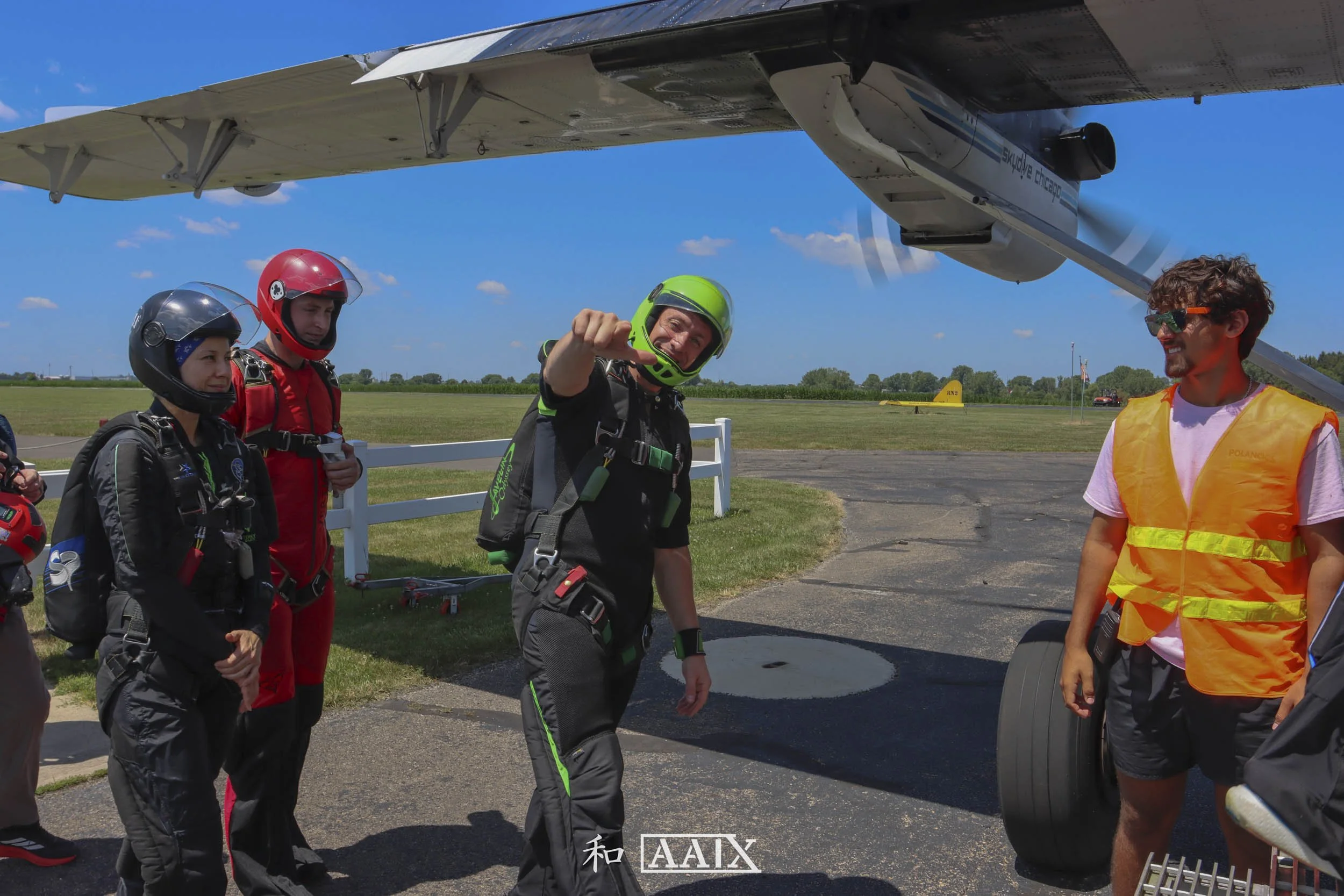 Group of skydivers in jumpsuits and helmets preparing for a jump near an airplane on a sunny day.