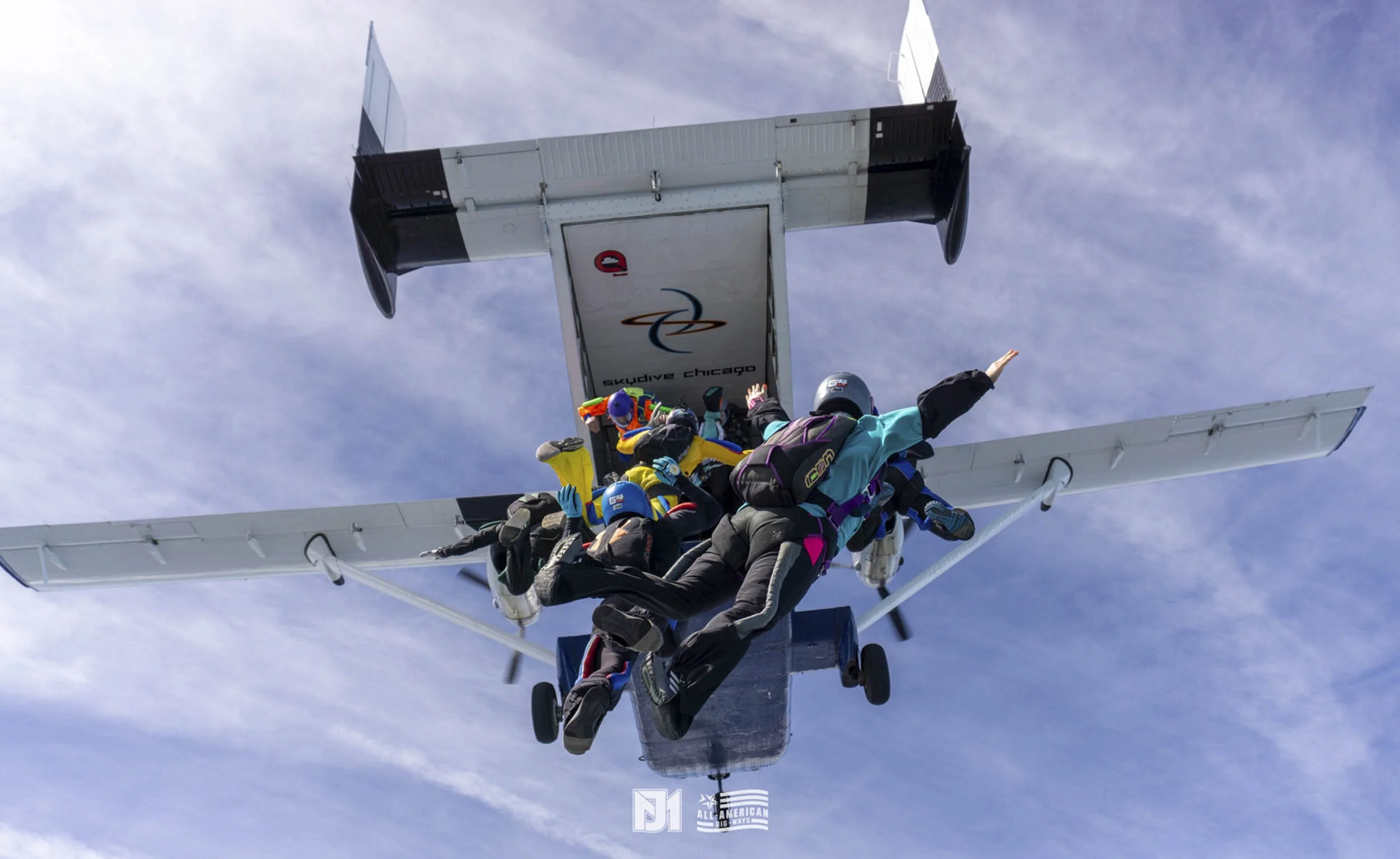 People skydiving out of a plane over Chicago sky, with some people in freefall and their parachutes deployed.