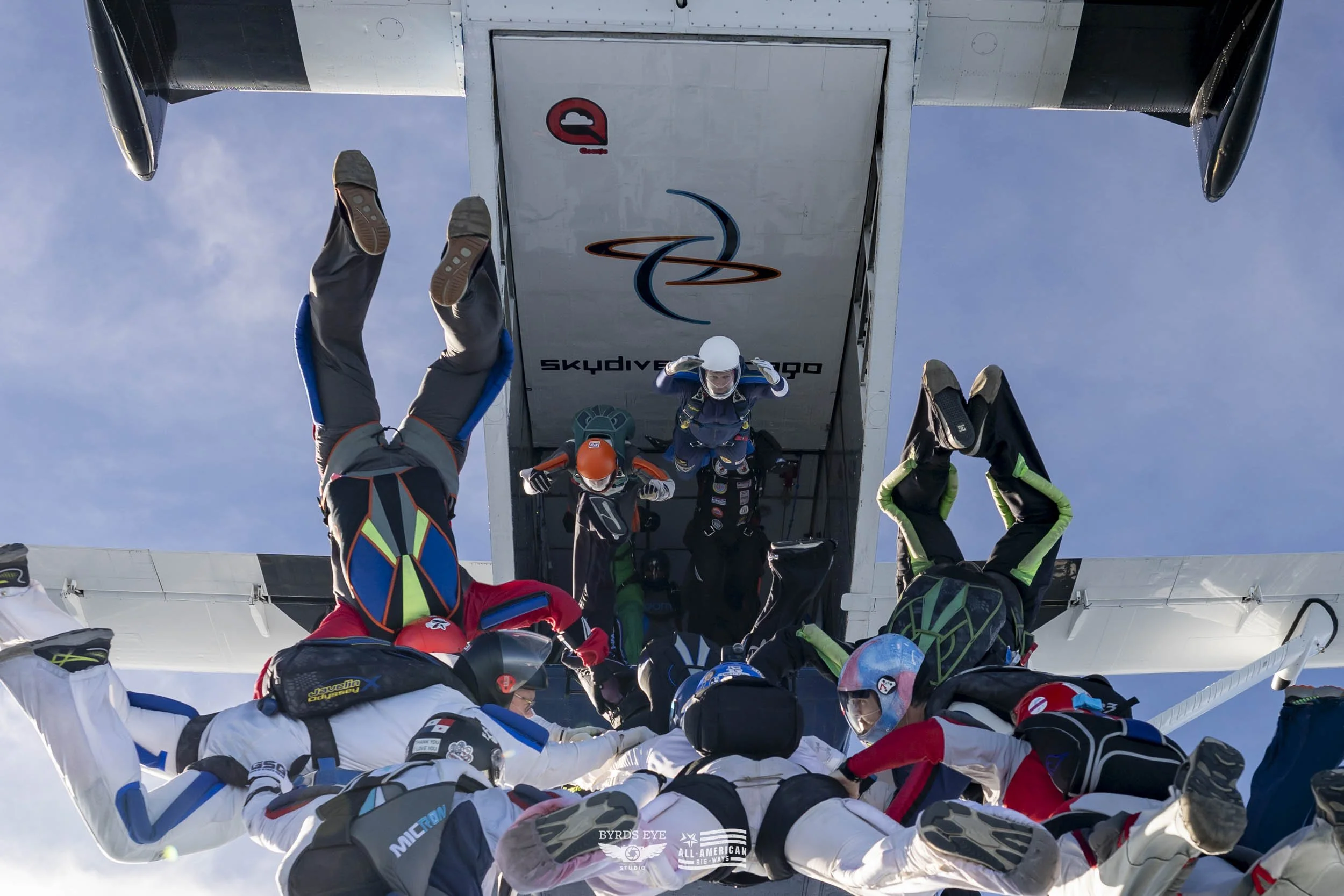 Skydivers exiting an aircraft with a clear blue sky background, preparing for free fall.