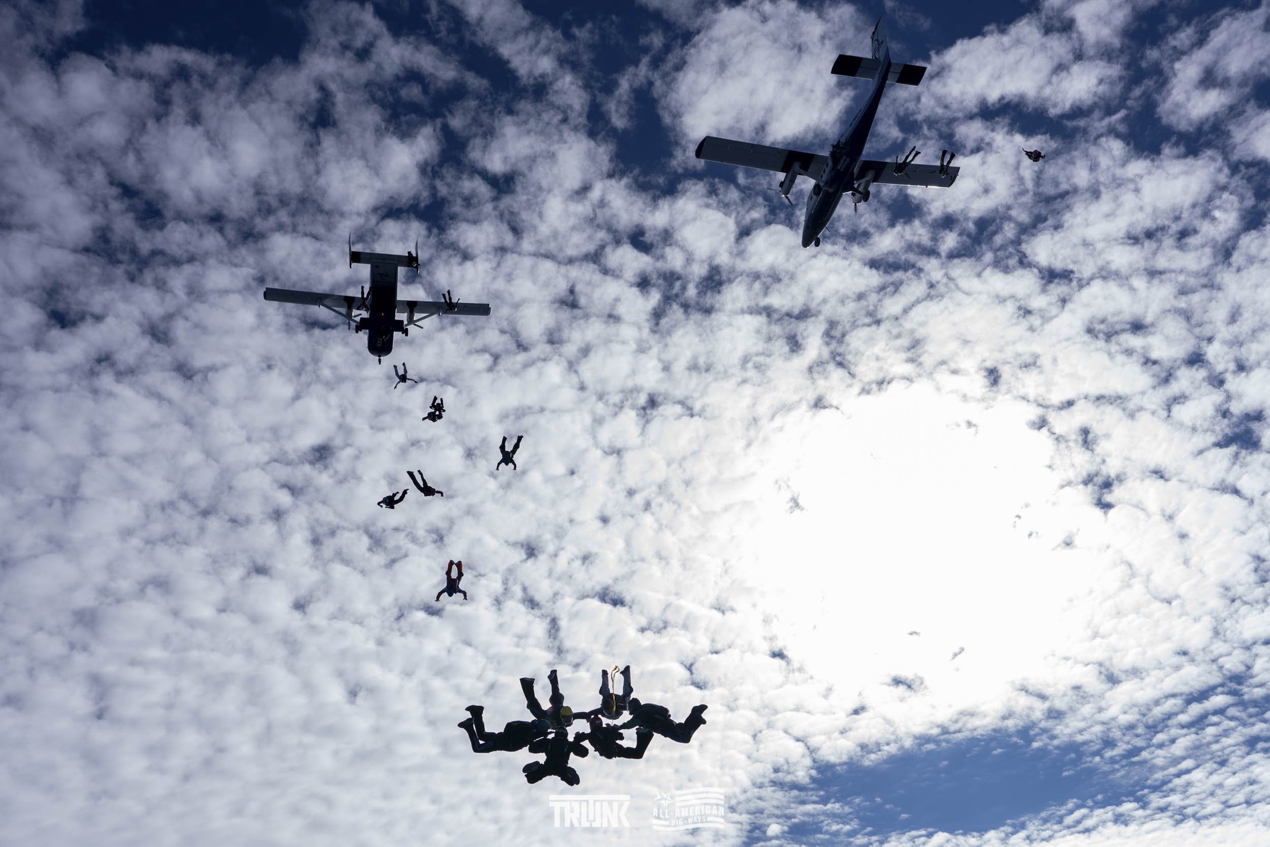Skydivers in free fall after jumping from aircrafts against a cloudy sky.