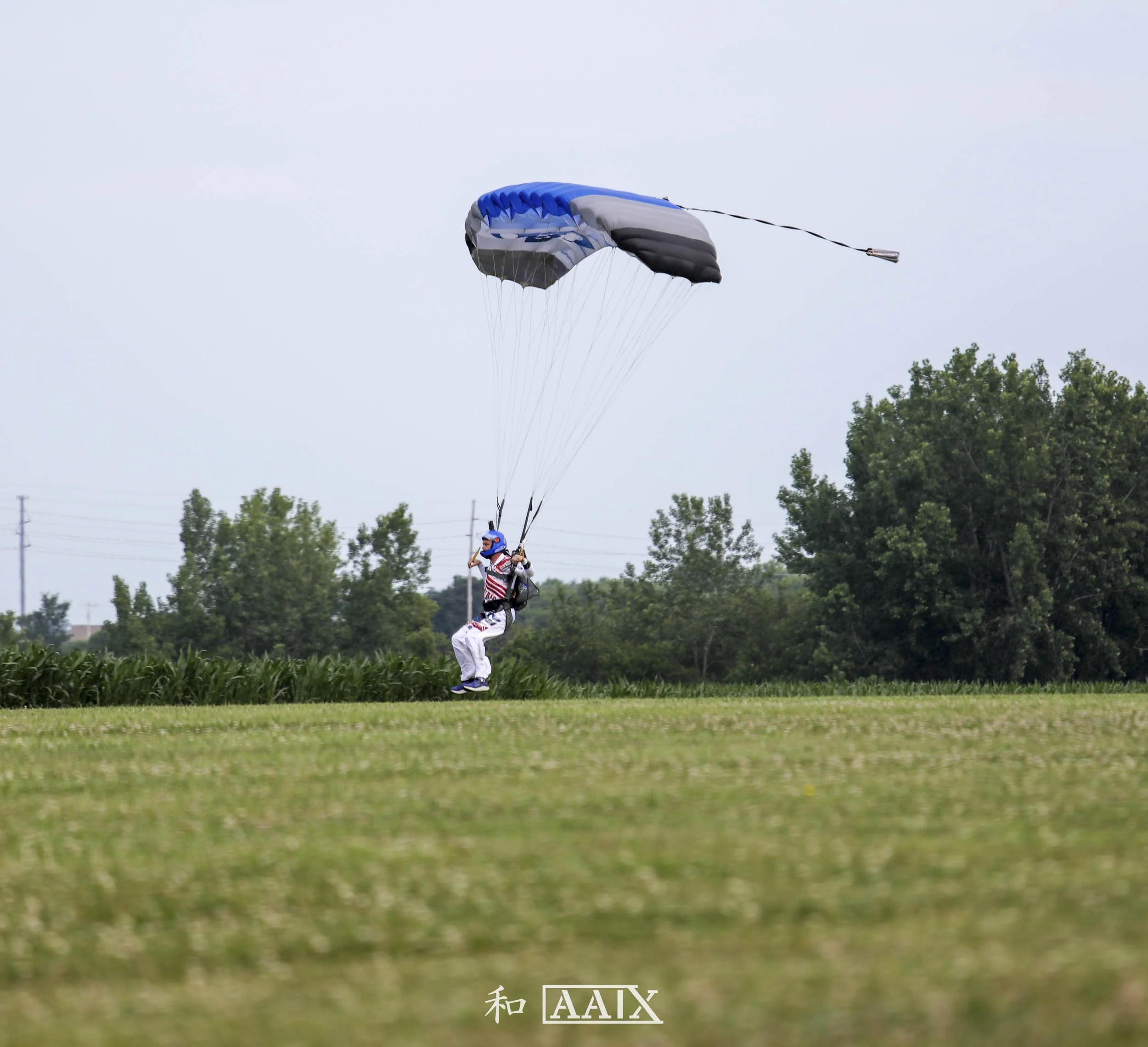 Person in patriotic clothing with a helmet jumping with a parachute over a grassy field.