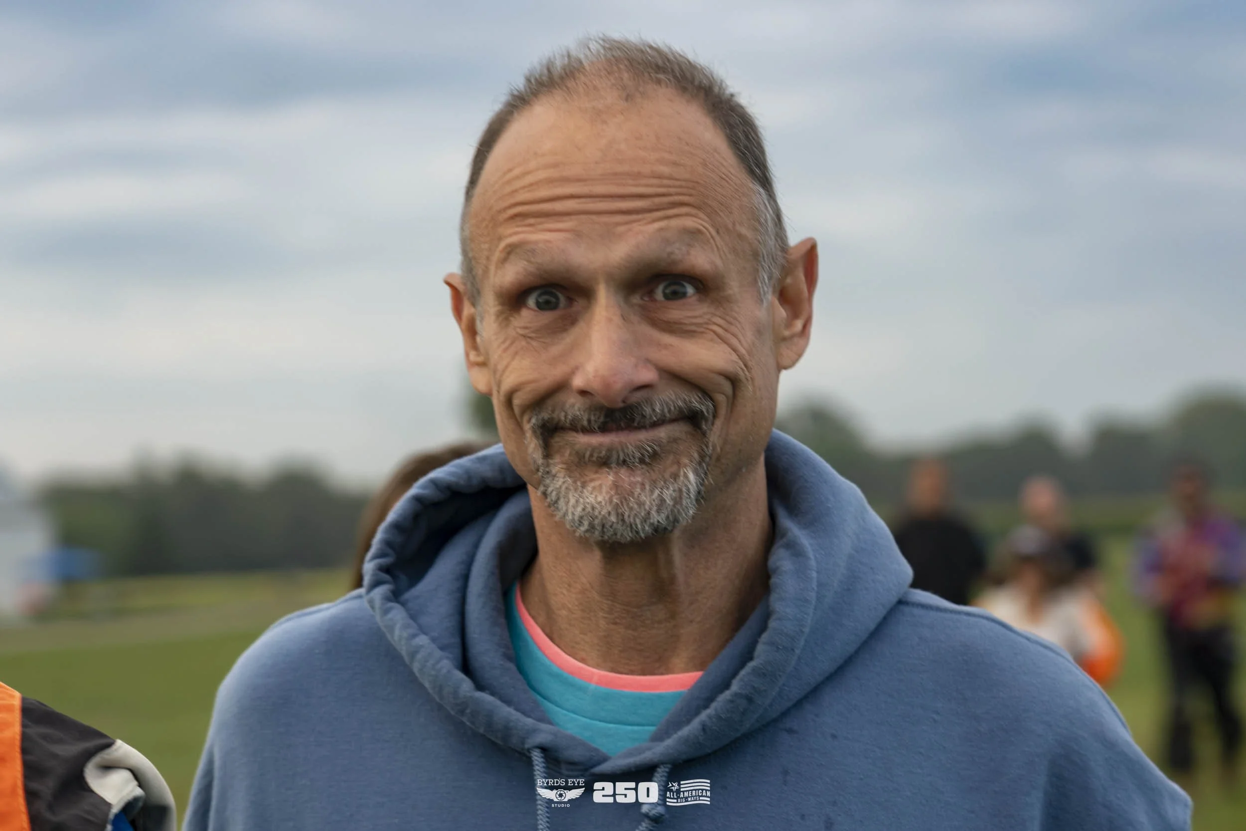 A middle-aged man with a slight smile and wide eyes wearing a blue hoodie.