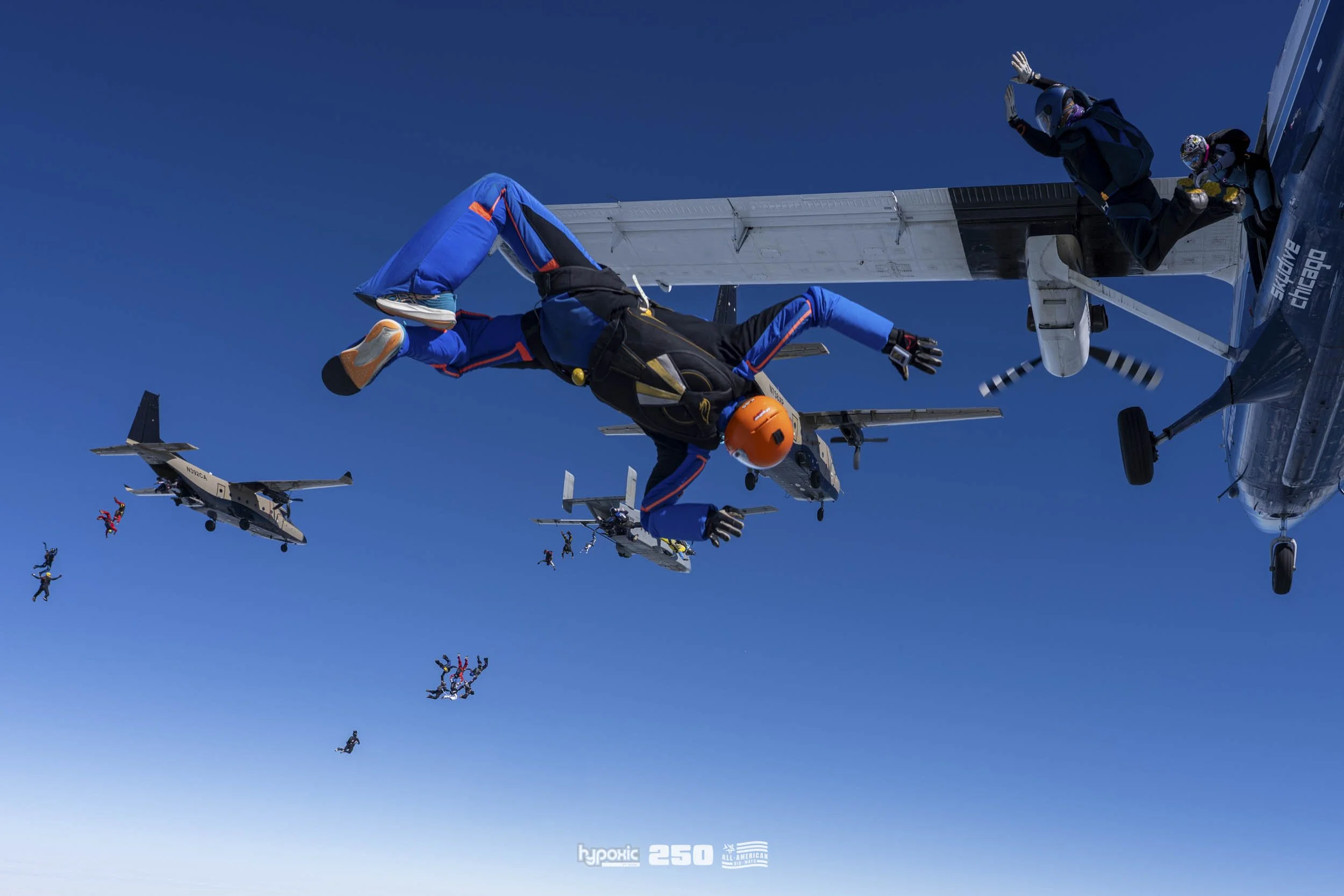 Skydivers jumping from aircraft with blue sky background.
