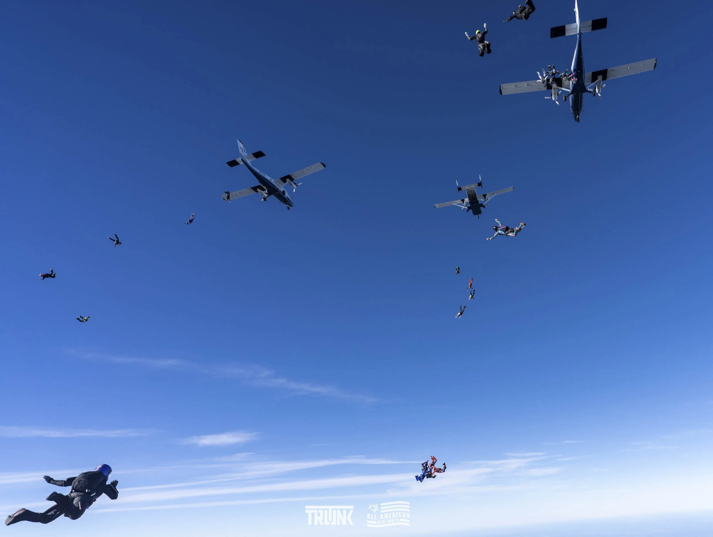 Skydivers jumping from aircraft in a clear blue sky.