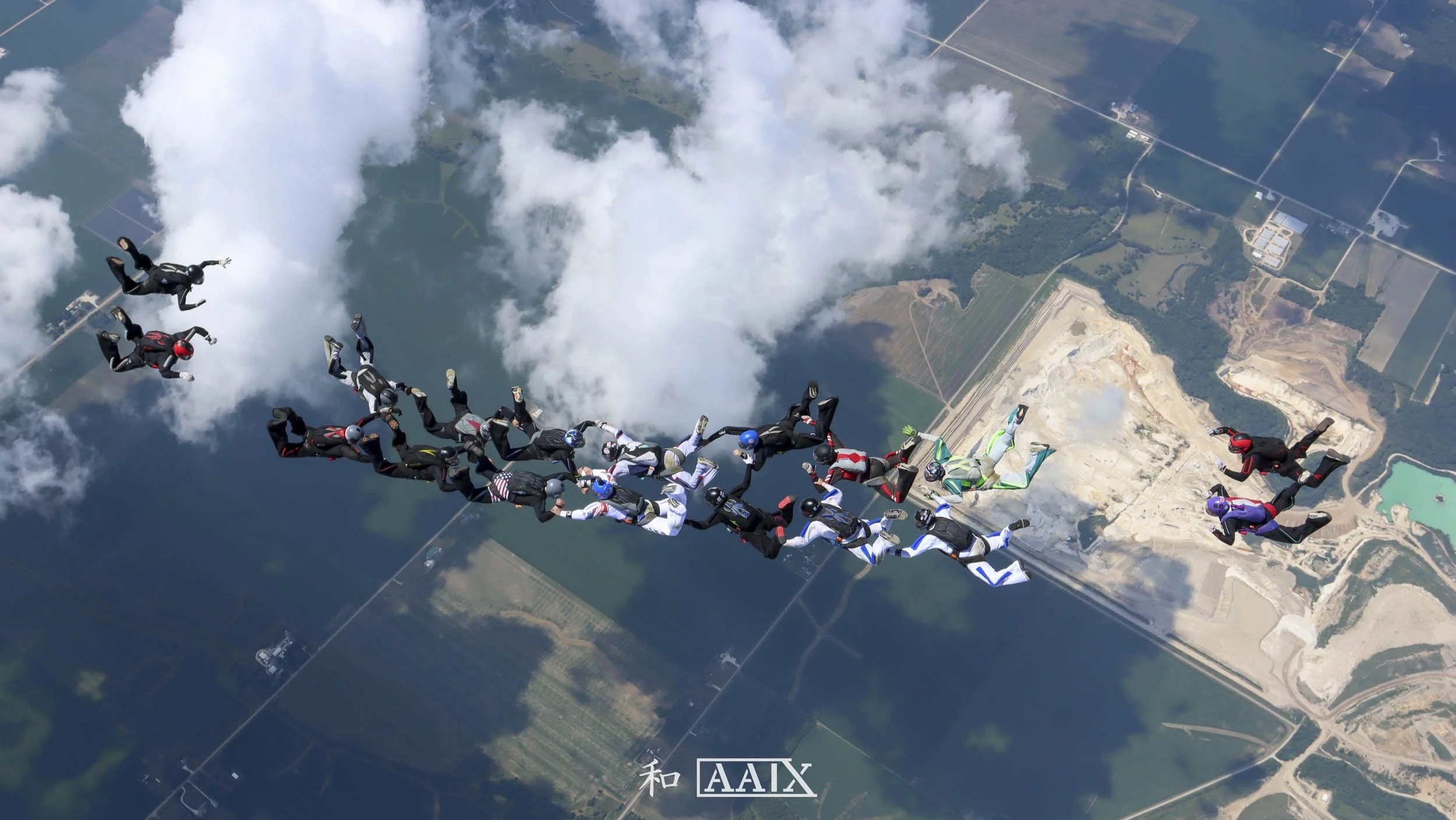 Group of skydivers forming a star shape in mid-air above farmland and clouds.
