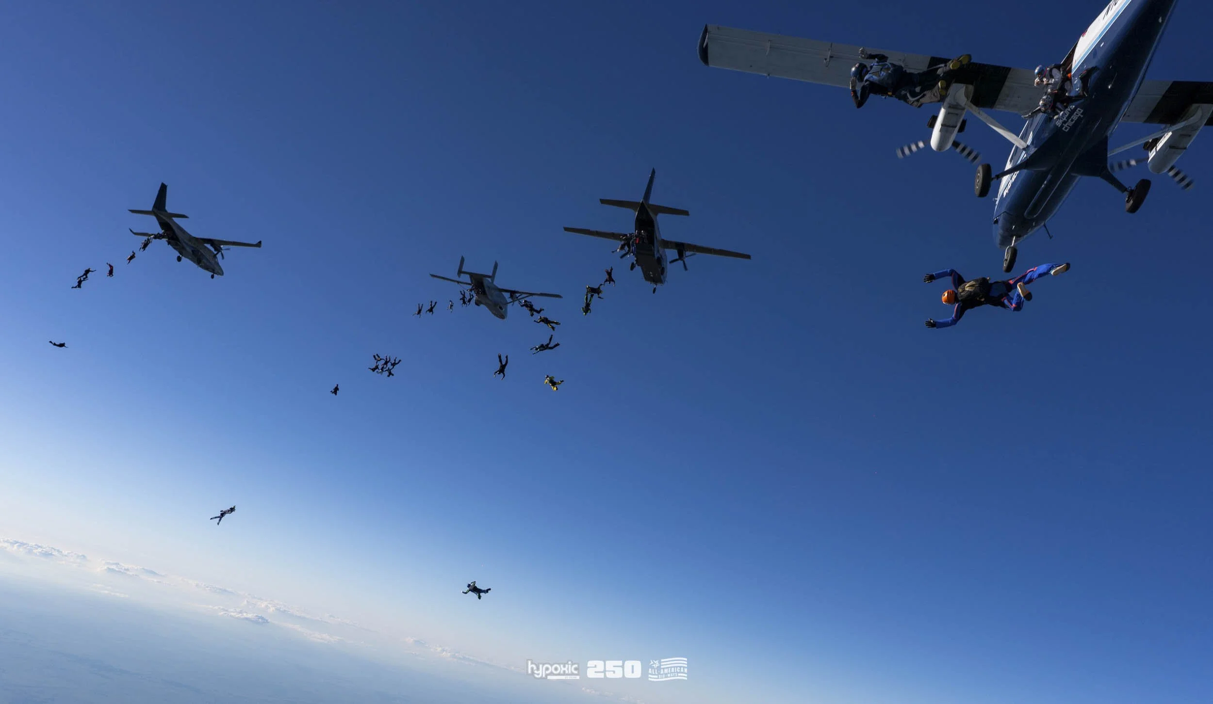Skydivers jumping from airplanes in formation against a blue sky during daytime.