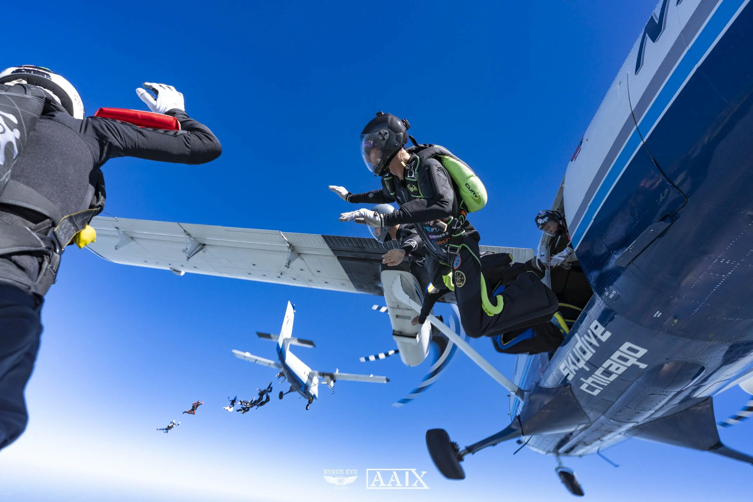 Skydivers jumping out of an airplane with blue sky in the background.