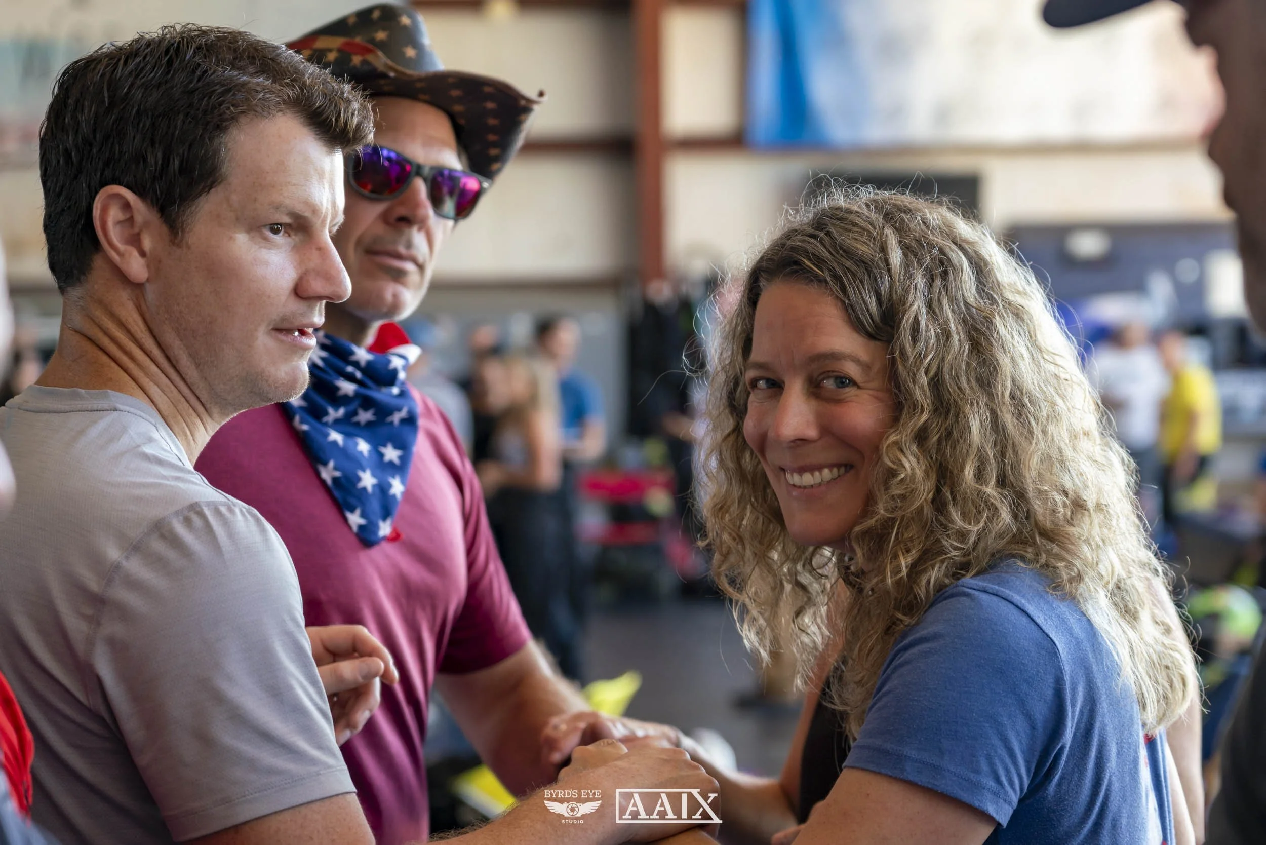 Four people talking and shaking hands at an indoor event, with blurred background and people in the background.