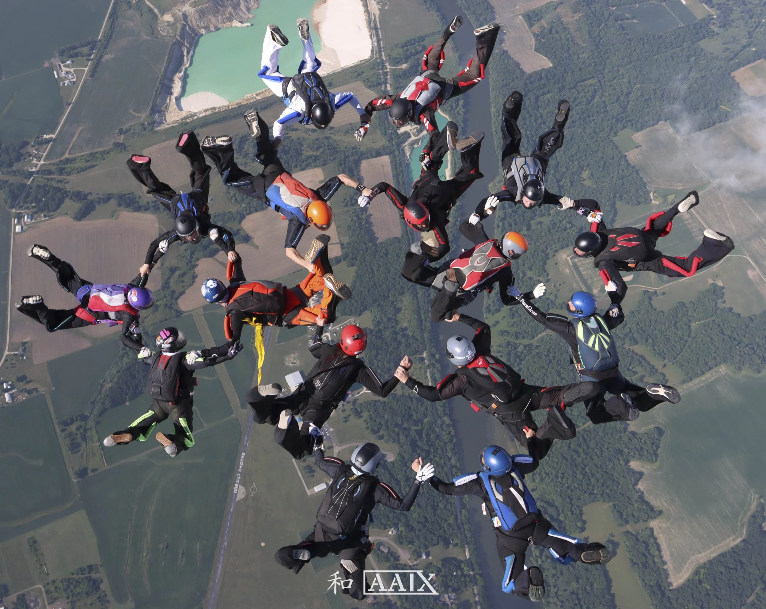 Group of skydivers forming a star shape skydiving above countryside, with fields, forests, and lakes below.