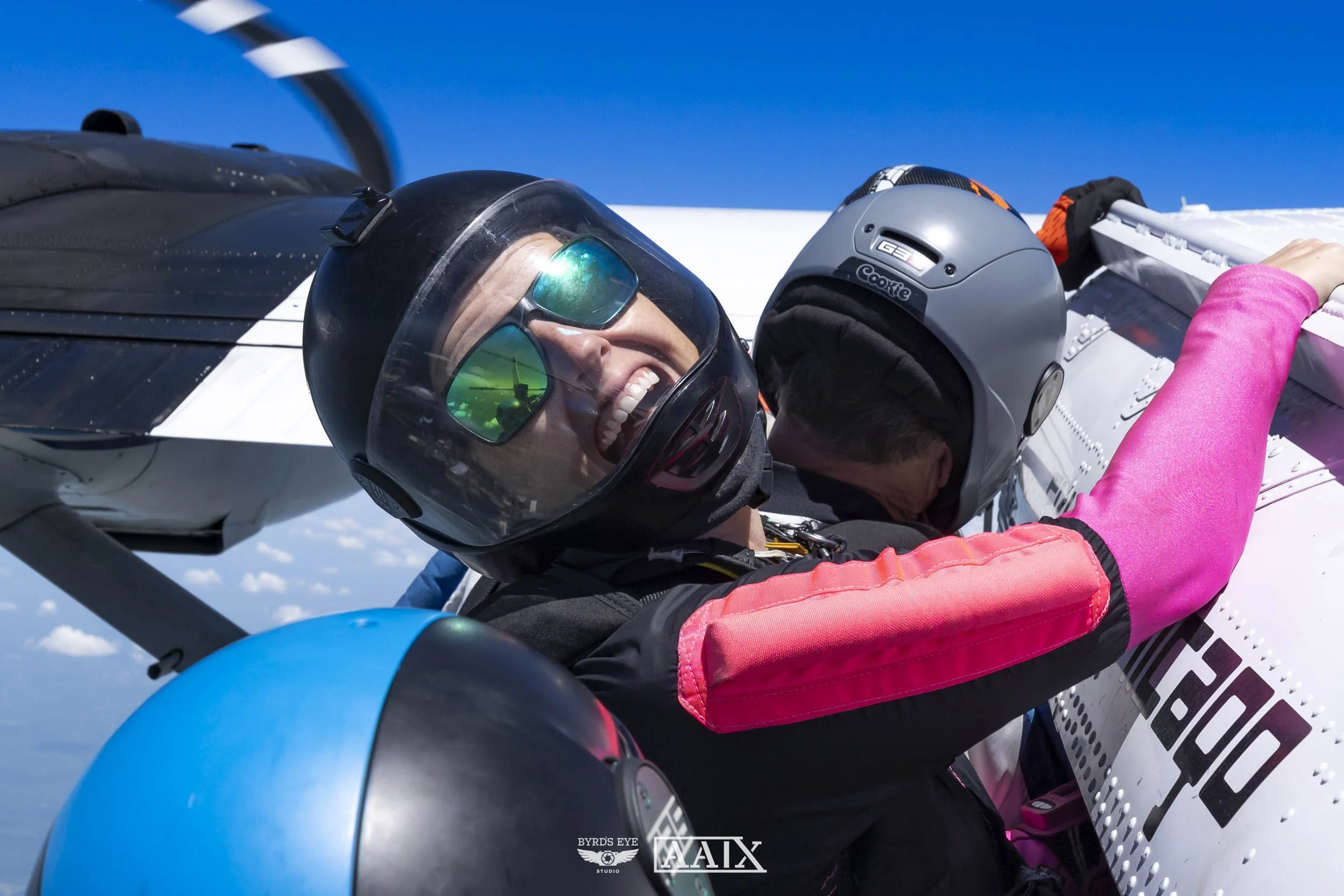 Two pilots in helmets preparing a fighter jet for flight against a bright blue sky.