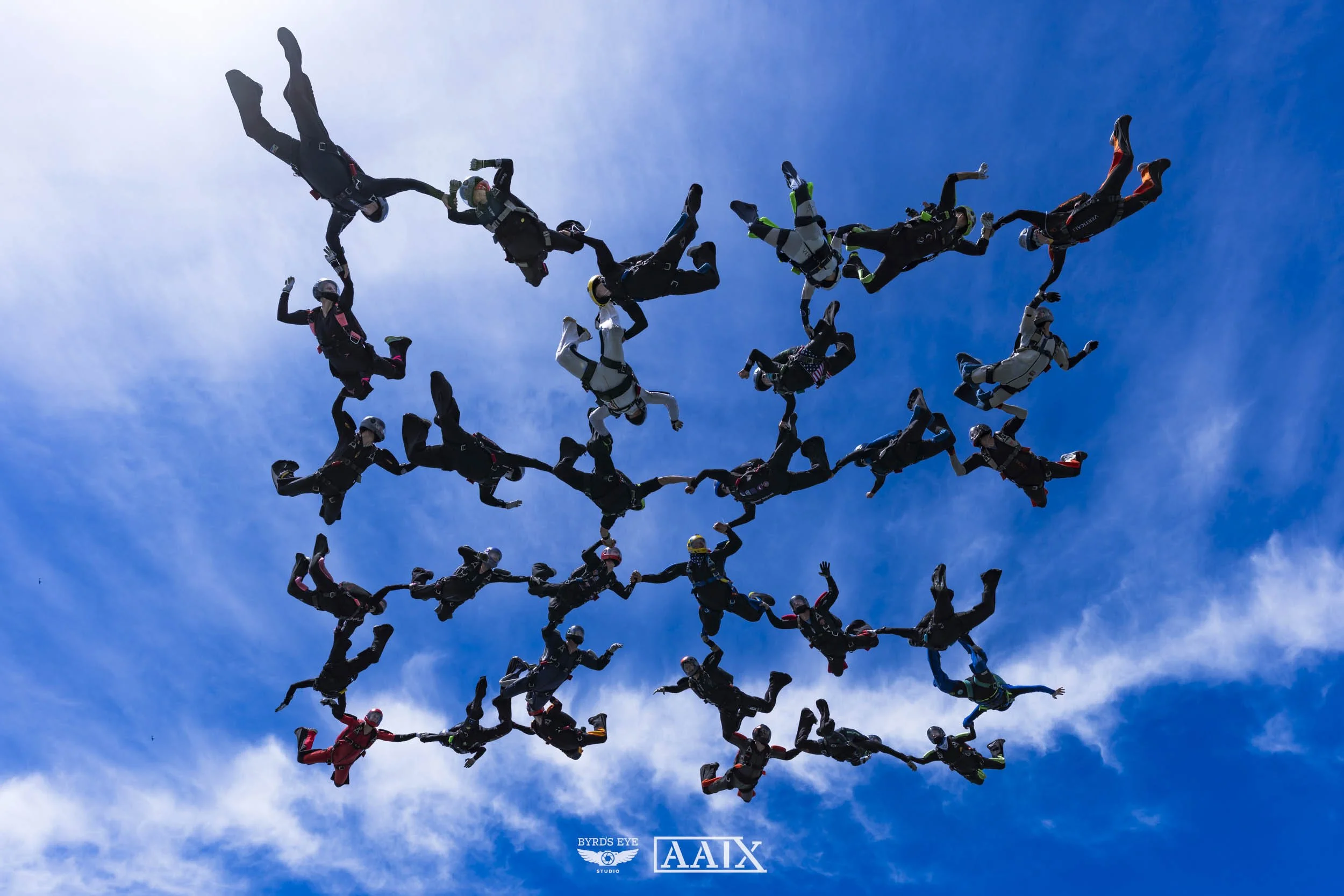 Group of skydivers forming a large connected human shape in the blue sky.