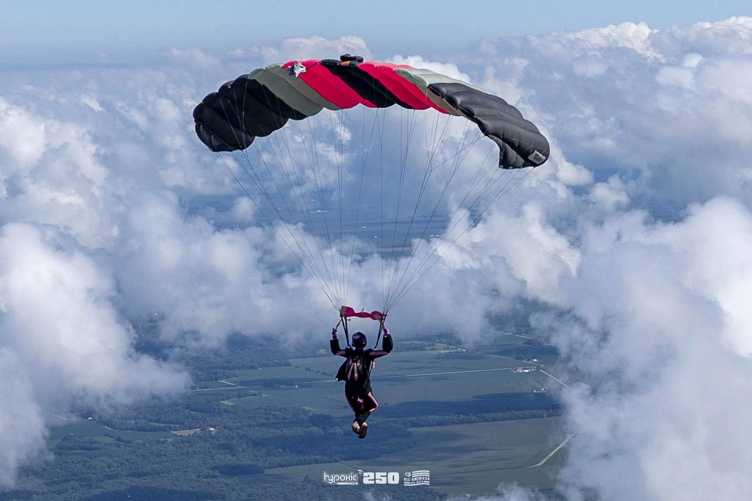 A person paragliding through the sky with clouds and a landscape below.