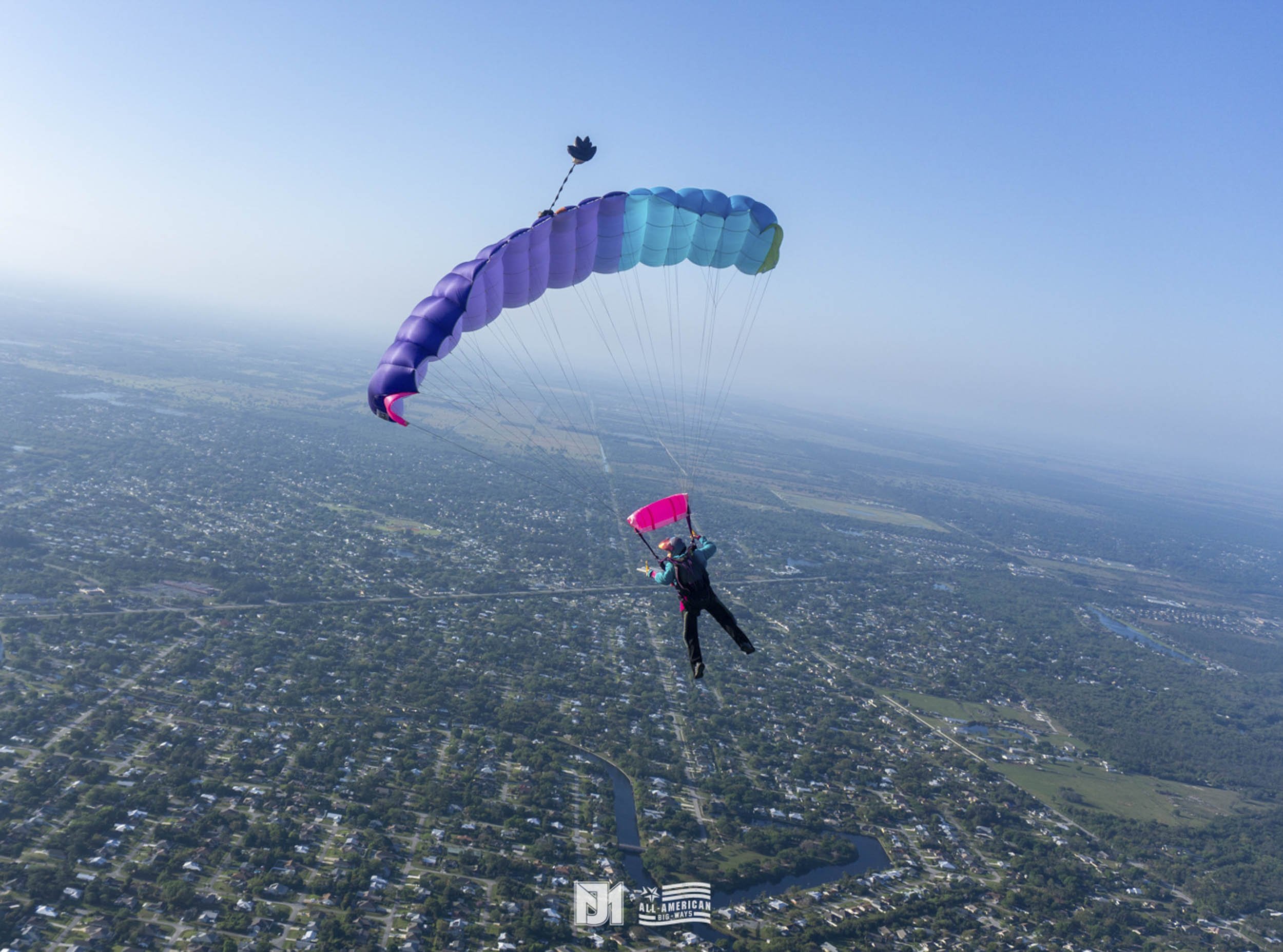 A person skydiving with a multicolored parachute over a cityscape.